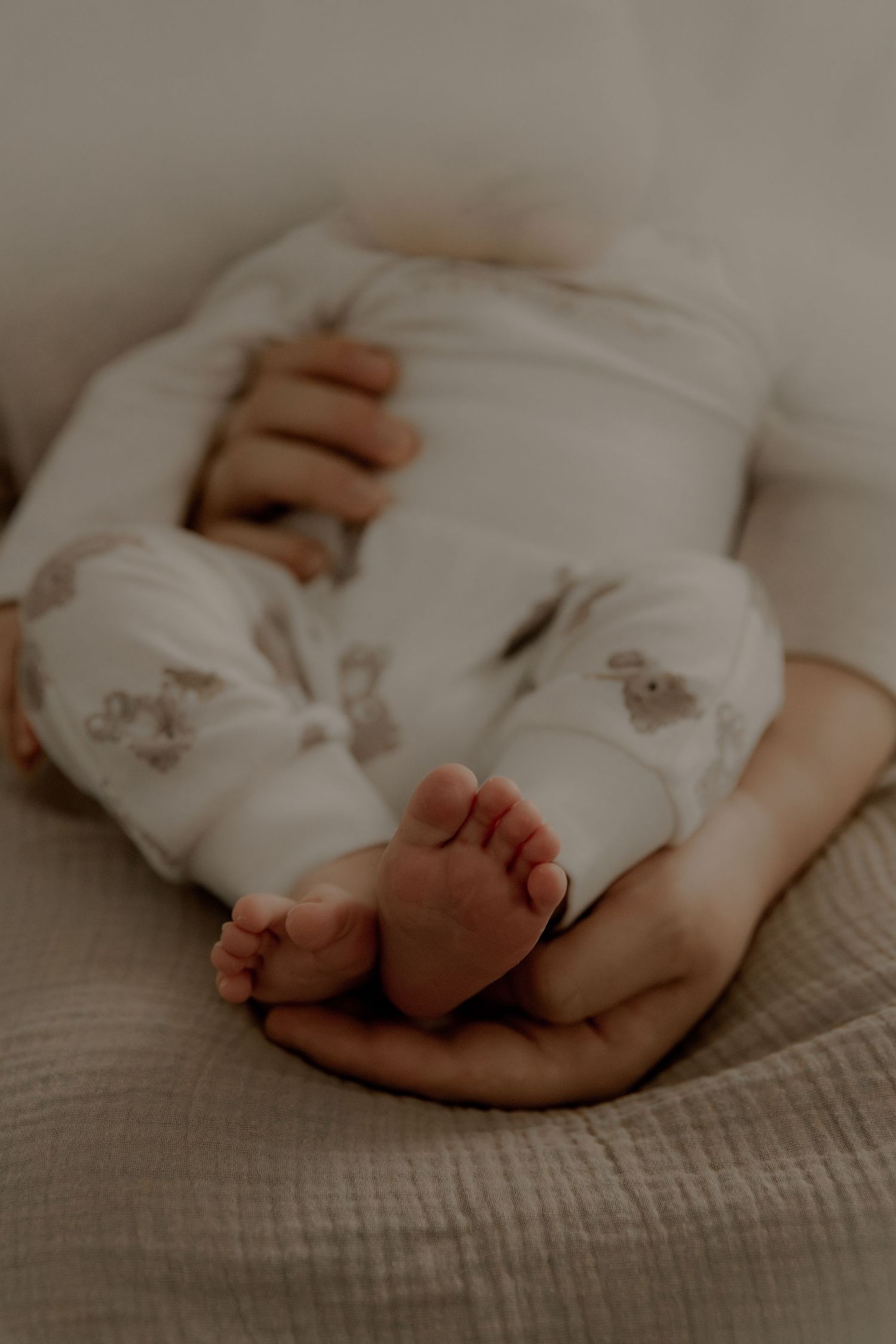 Newborn feet resting in adult hands on beige linen fabric.