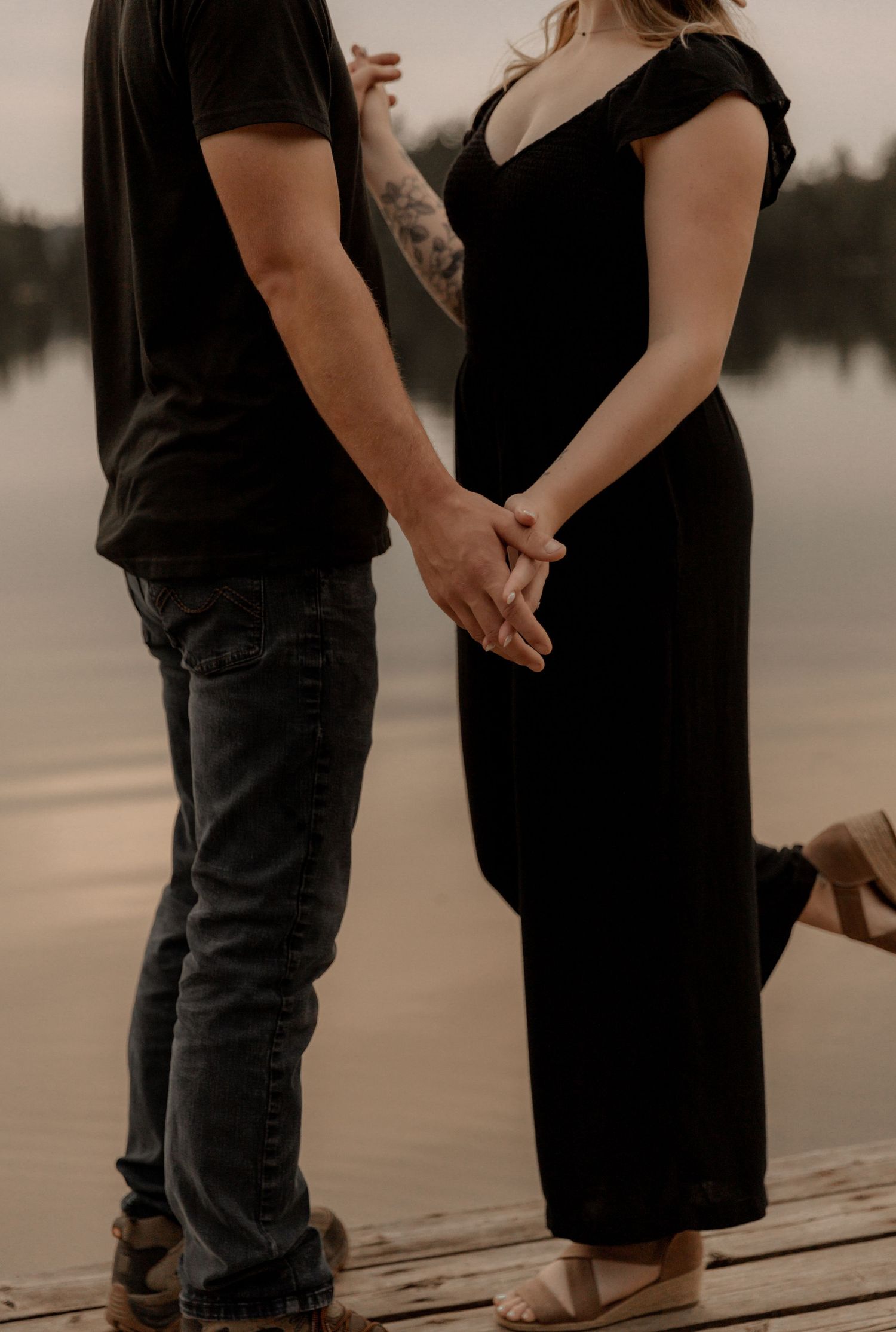 Couple holding hands on dock during sunset engagement photoshoot.
