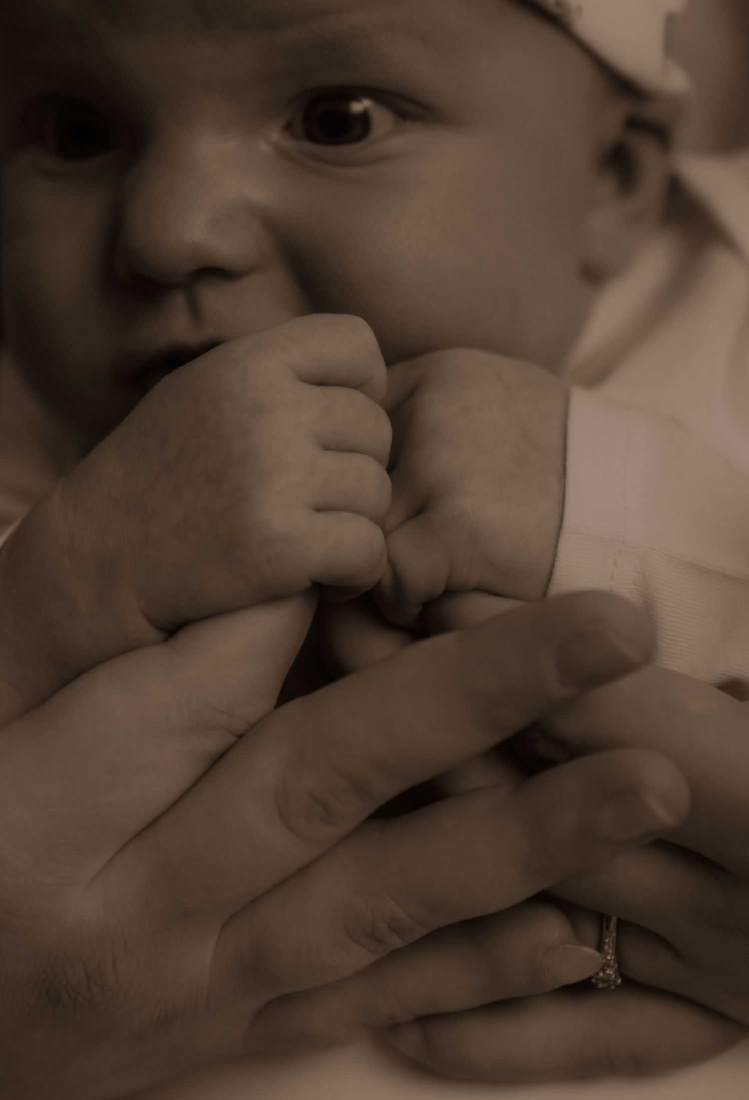 Sepia-toned close-up photo of a young child's face being held by gentle hands with a ring.