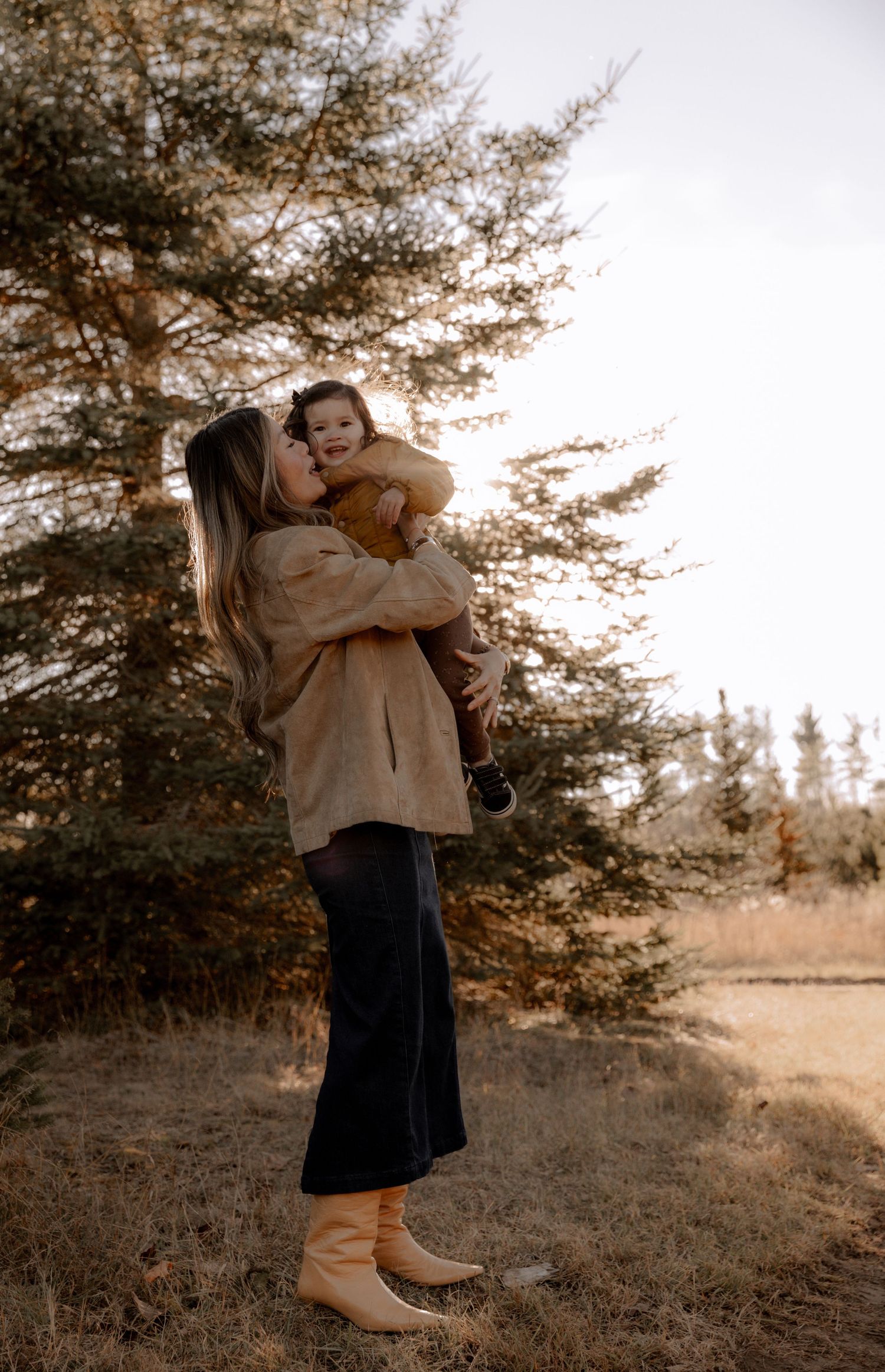 A tender moment between parent and child in a cozy fall setting with warm earth tones and pine trees.