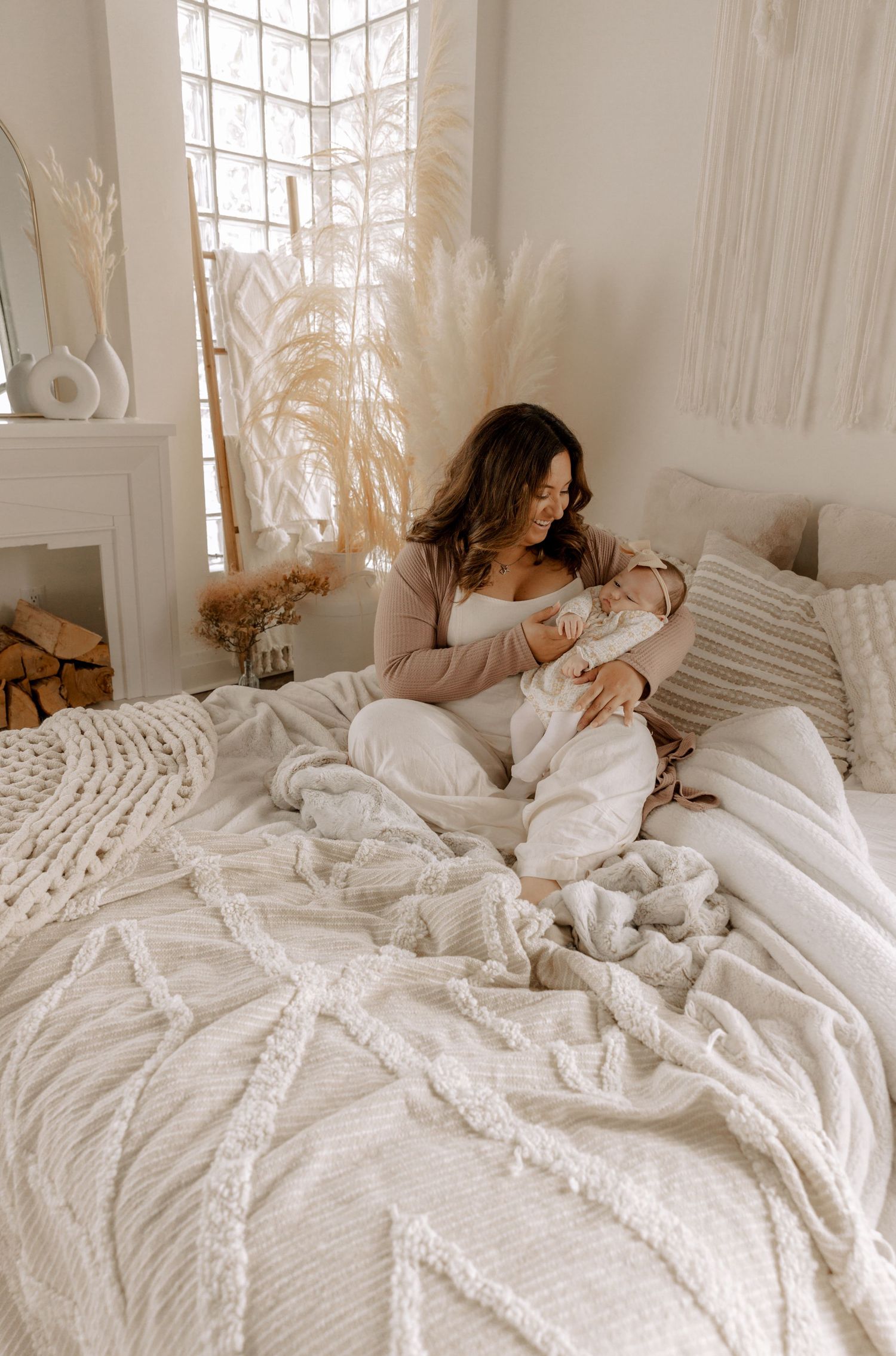 A cozy bedroom scene with textured white bedding and pampas grass decor by a bright corner window.