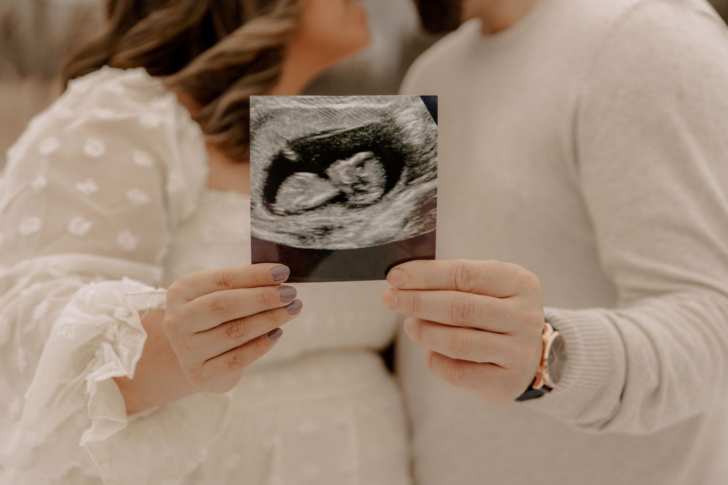 Hands holding a black and white ultrasound sonogram photo showing details of an unborn baby.