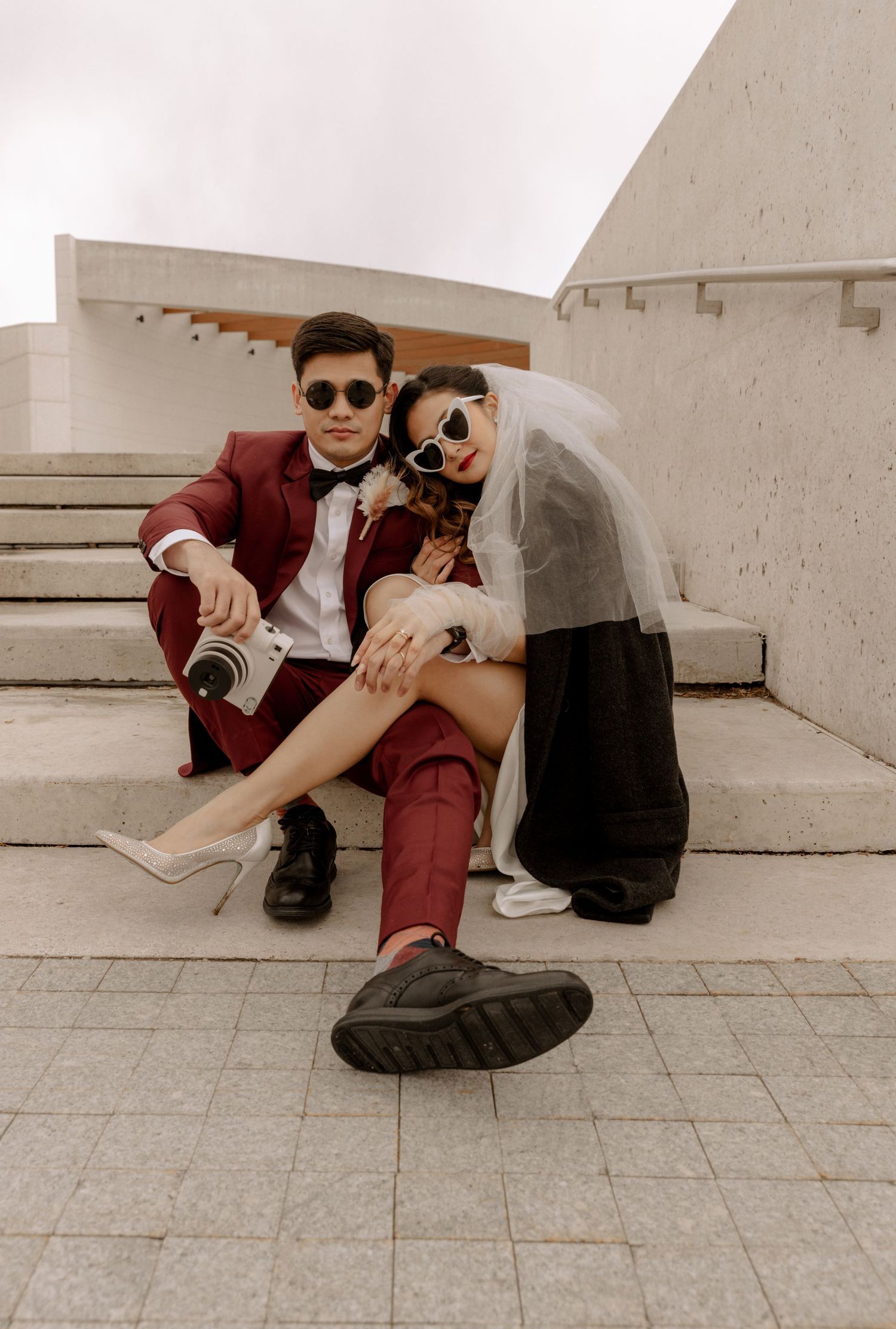 Retro wedding photoshoot on concrete stairs with couple in sunglasses and burgundy suit.