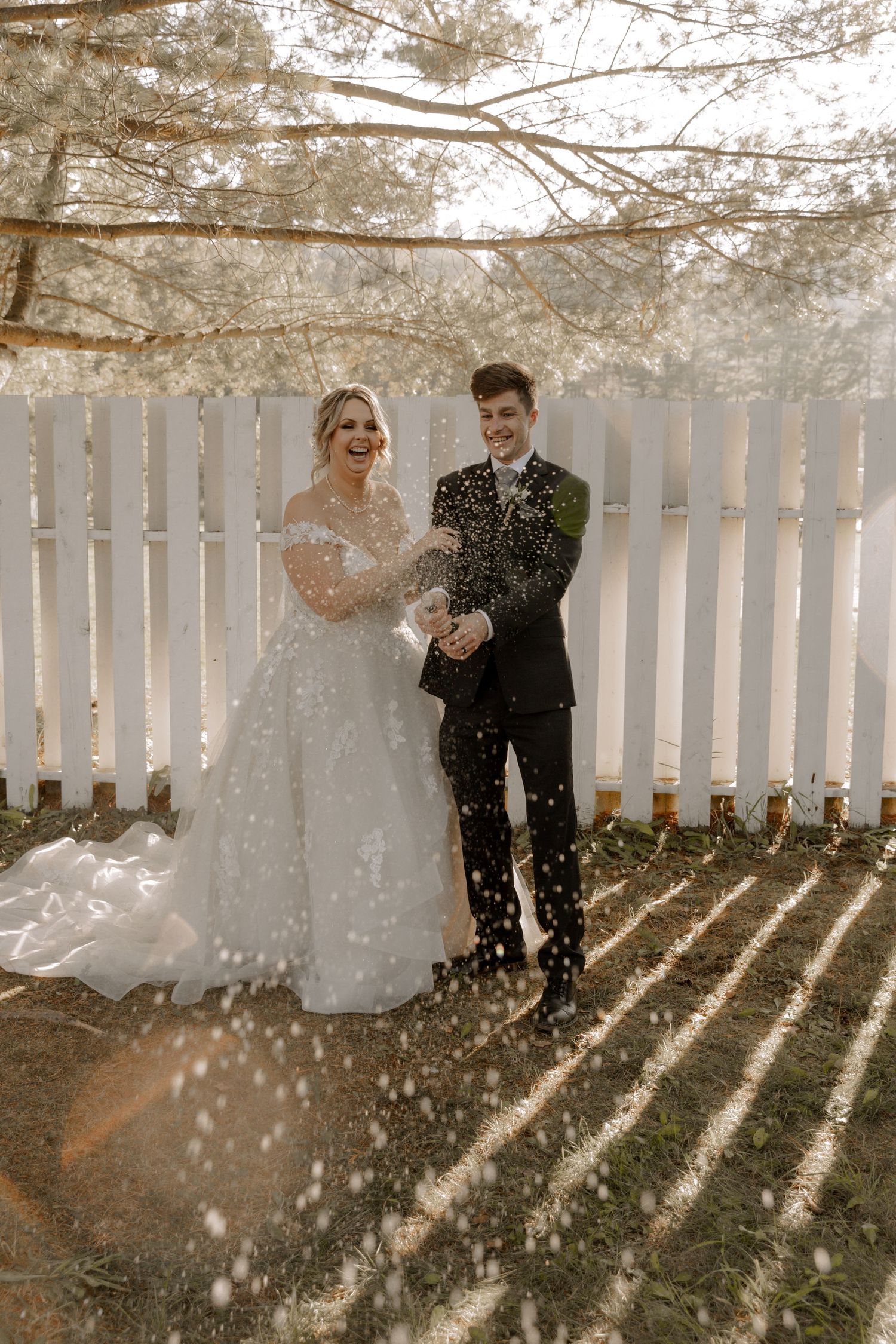 A winter wedding portrait with sparkles of light falling against a white fence backdrop.