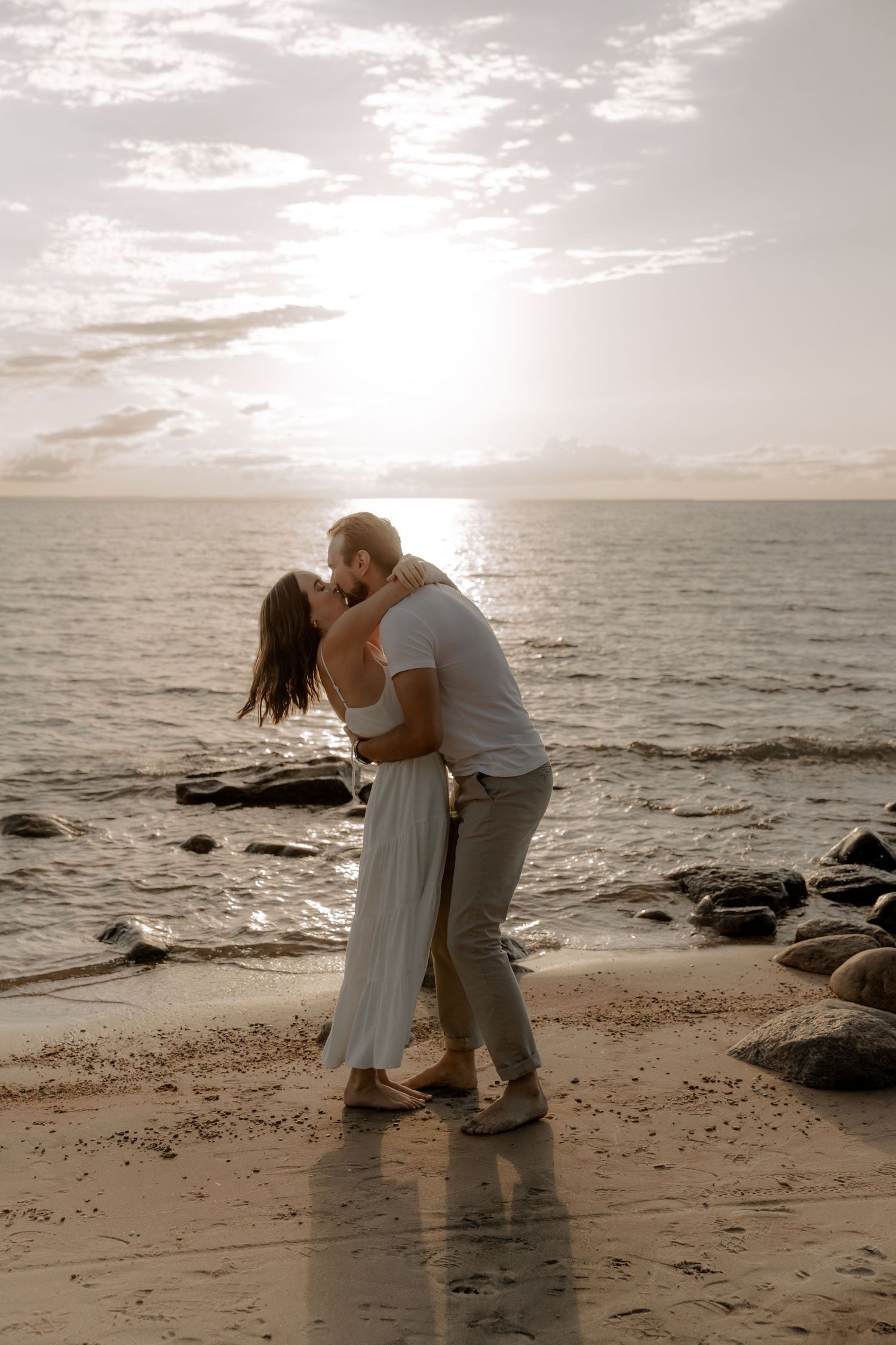 A loving couple shares a romantic moment on a rocky beach during golden hour.