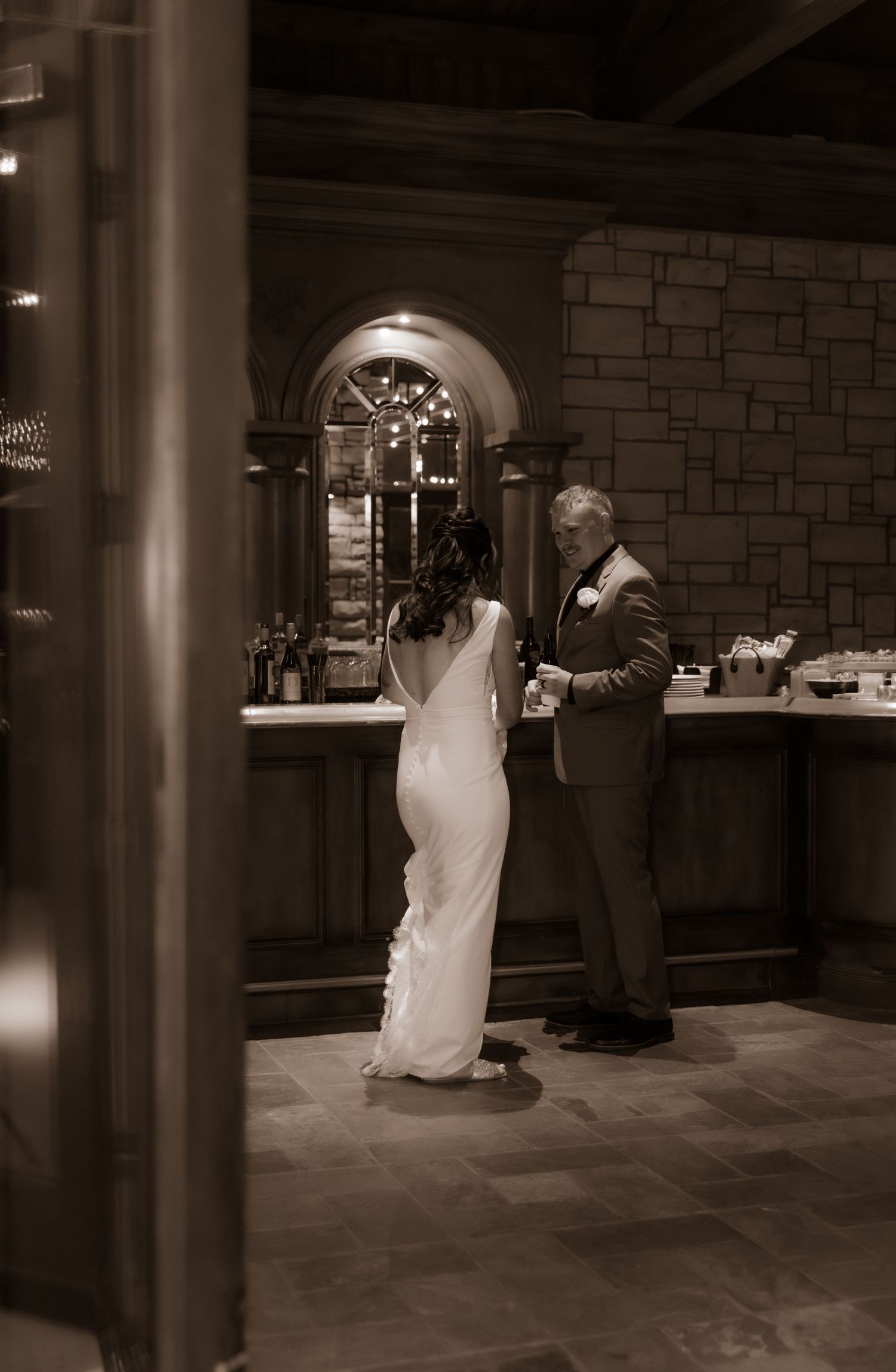 Bride and groom at a rustic stone bar during their wedding celebration.