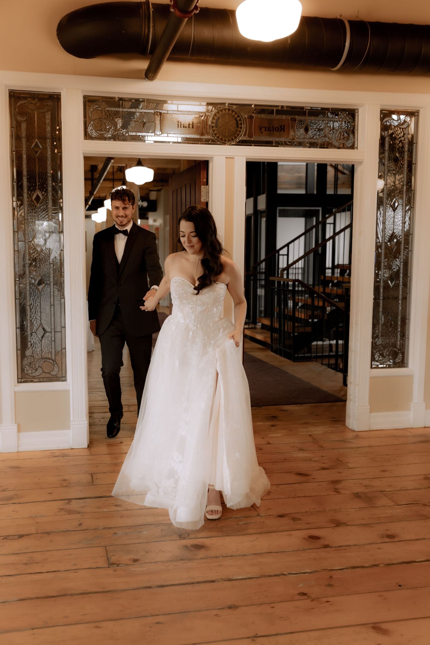 Wedding couple walking through an elegant hallway with wooden floors and decorative panels.