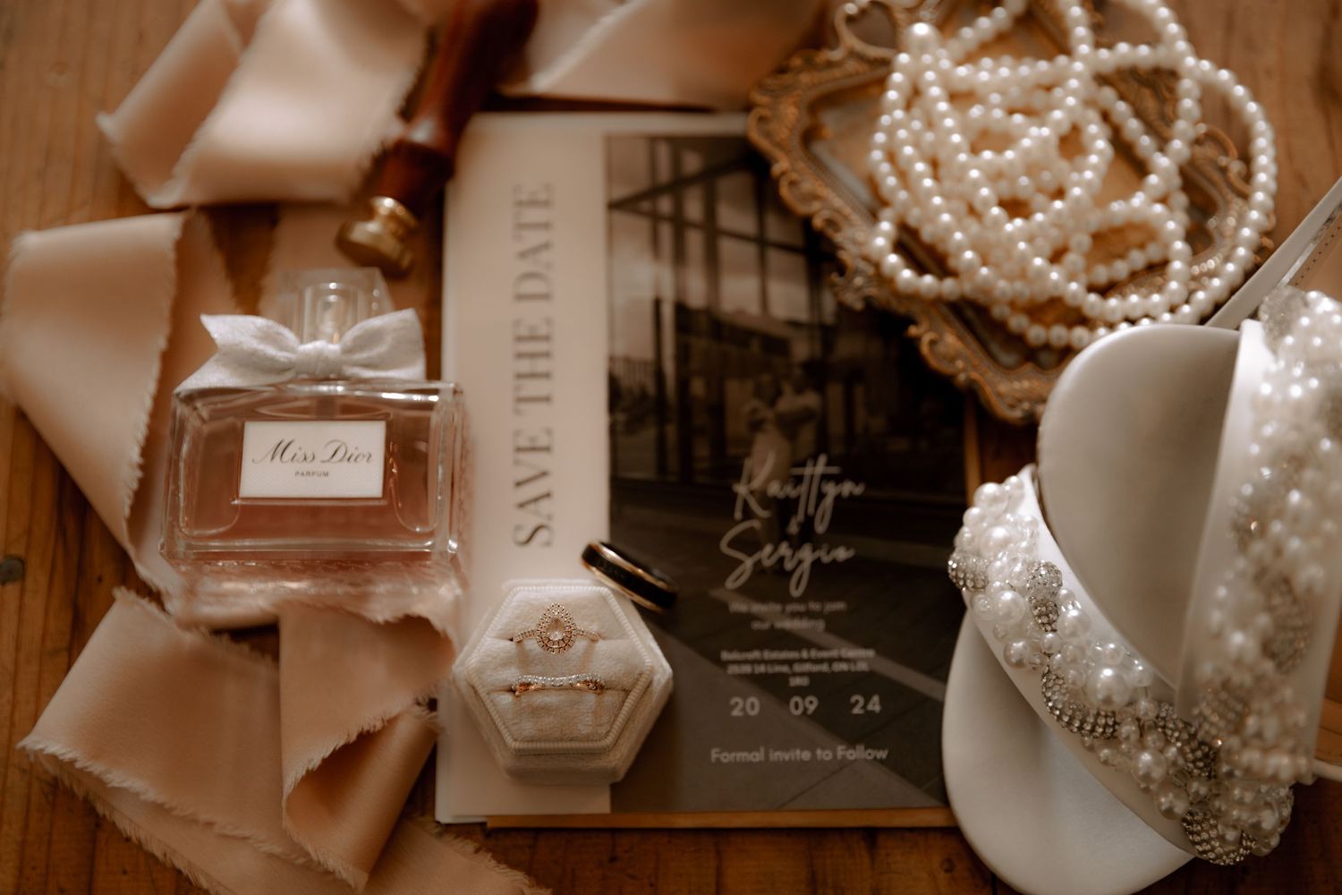 Wedding accessories including perfume bottle, pearls, and book arranged on wooden surface.