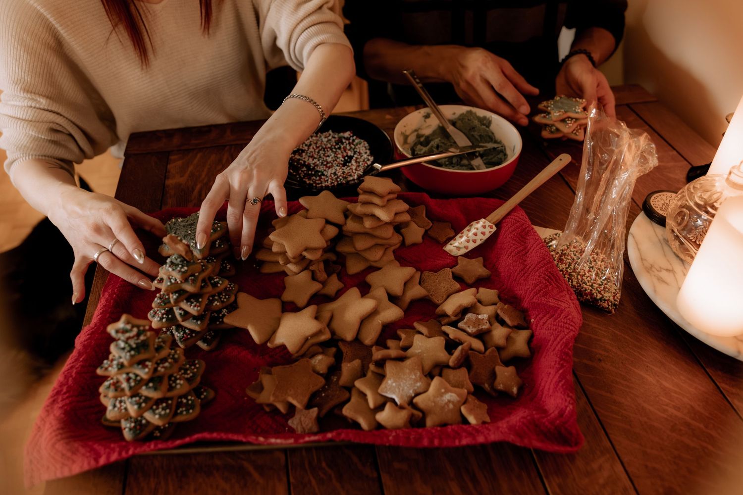 Holiday treats and decorative pinecones arranged on a red cloth with candlelight.