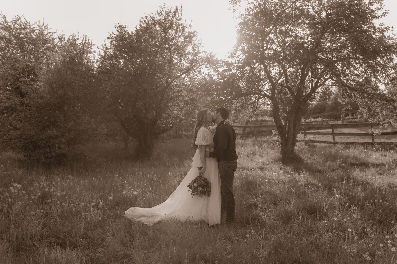 Sepia-toned wedding photo of a couple standing in an orchard field.