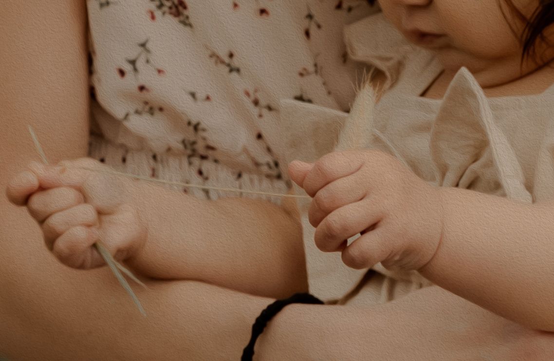 Close-up shot of small hands holding a delicate string or thread against a floral background.