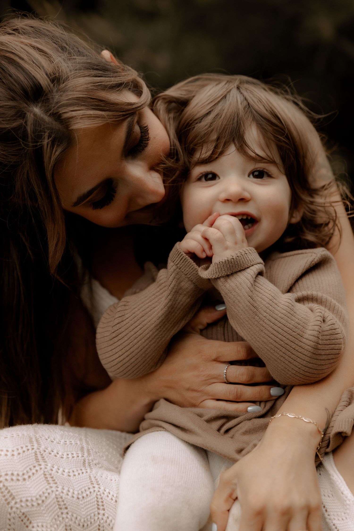 A sweet candid moment between parent and toddler wearing matching beige sweaters captured in warm moody lighting.