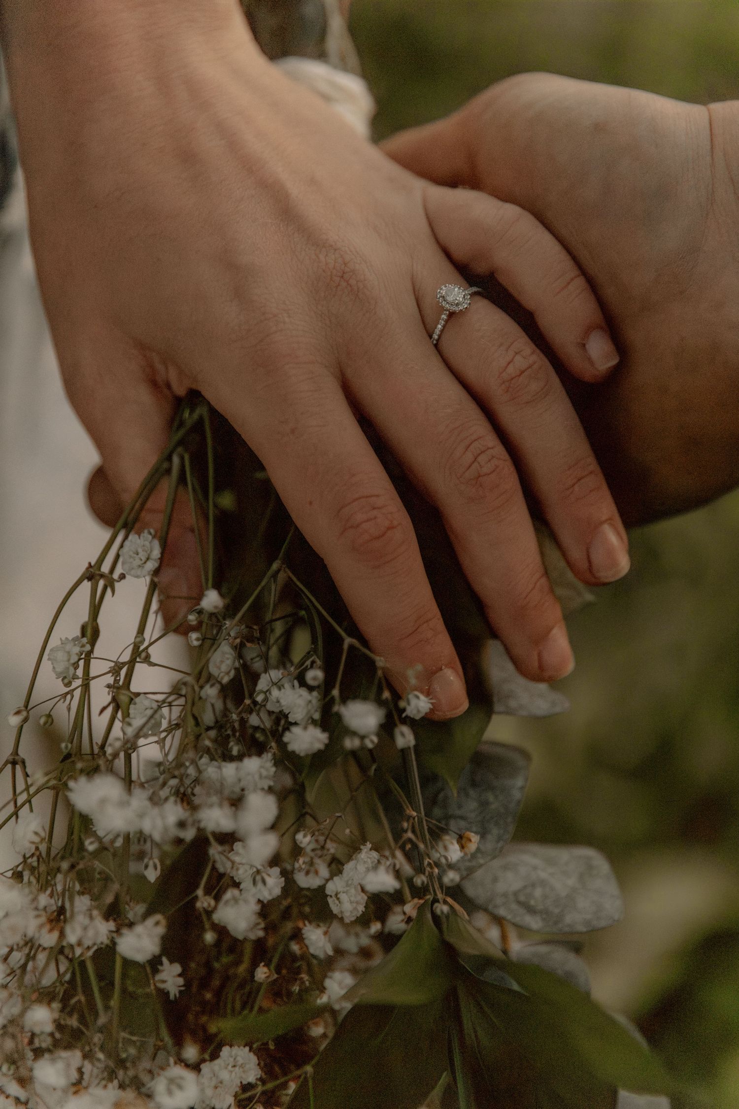 Elegant engagement ring sparkles as hands hold baby's breath flowers.