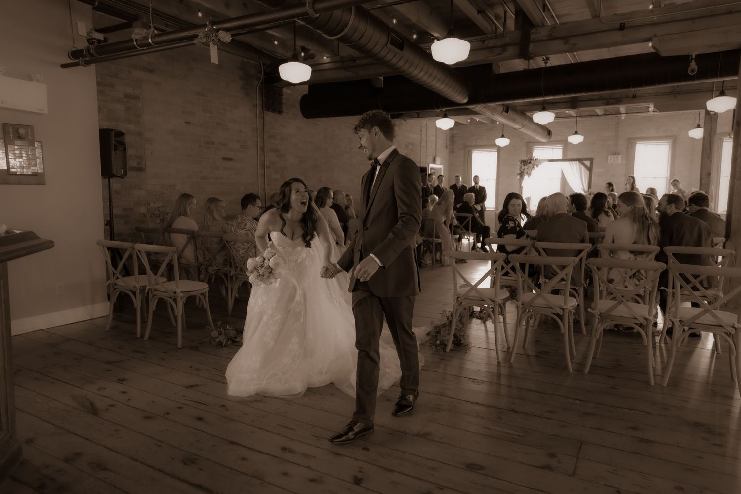 A sepia-toned wedding scene in a rustic venue featuring exposed brick walls and vintage-style decor.