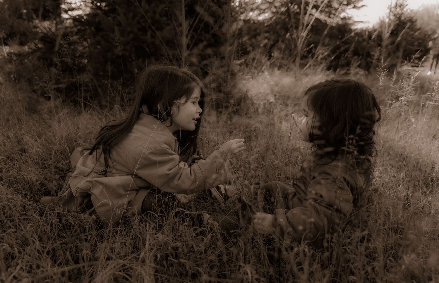 Two figures sitting in a meadow captured in sepia tones with natural foliage surroundings.