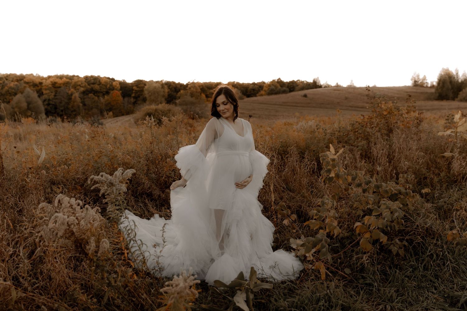 Moody portrait of wedding dress silhouetted against autumn landscape at dusk.