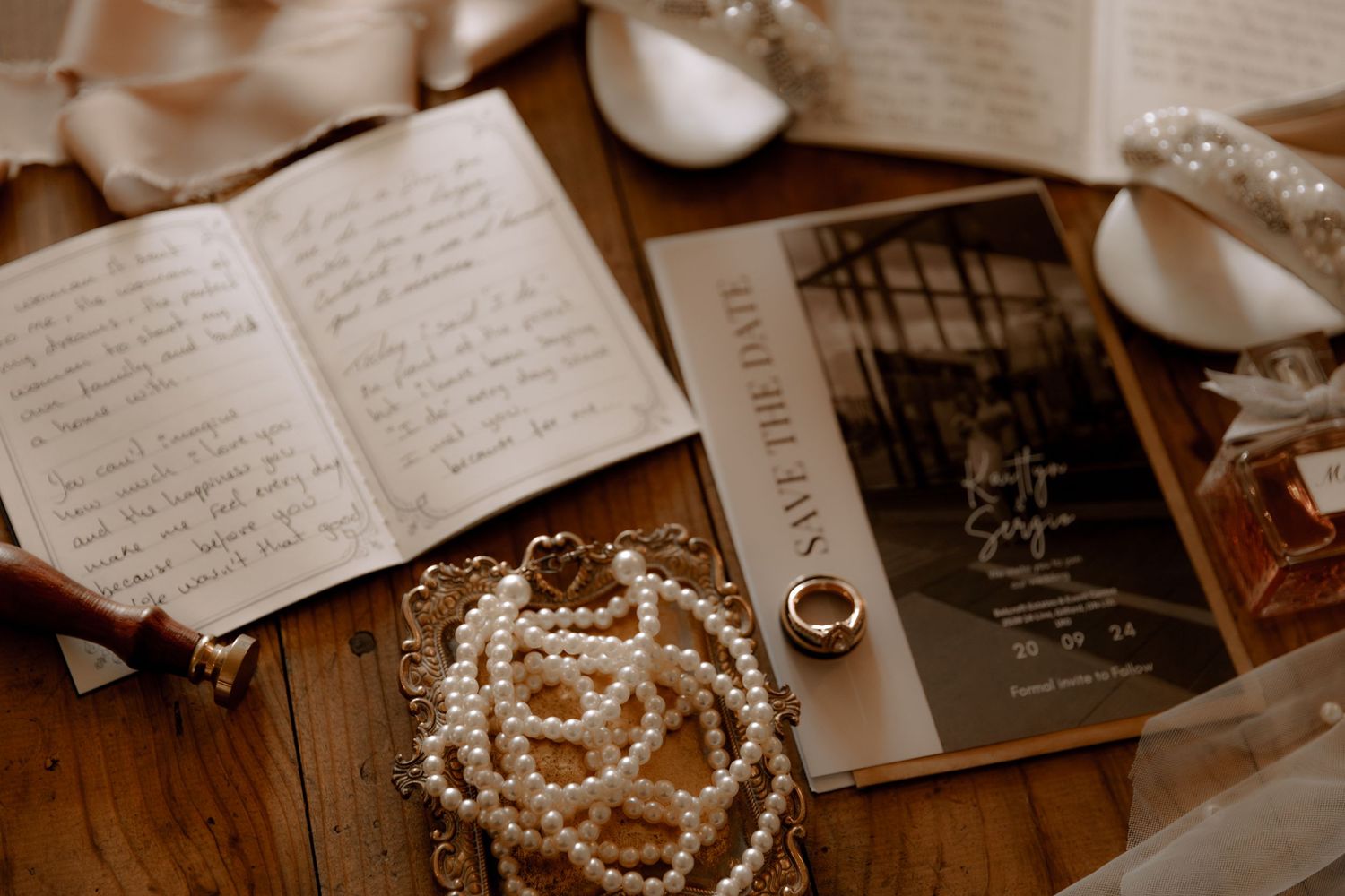 Open journal with handwritten notes beside wedding invitation and pearl jewelry.