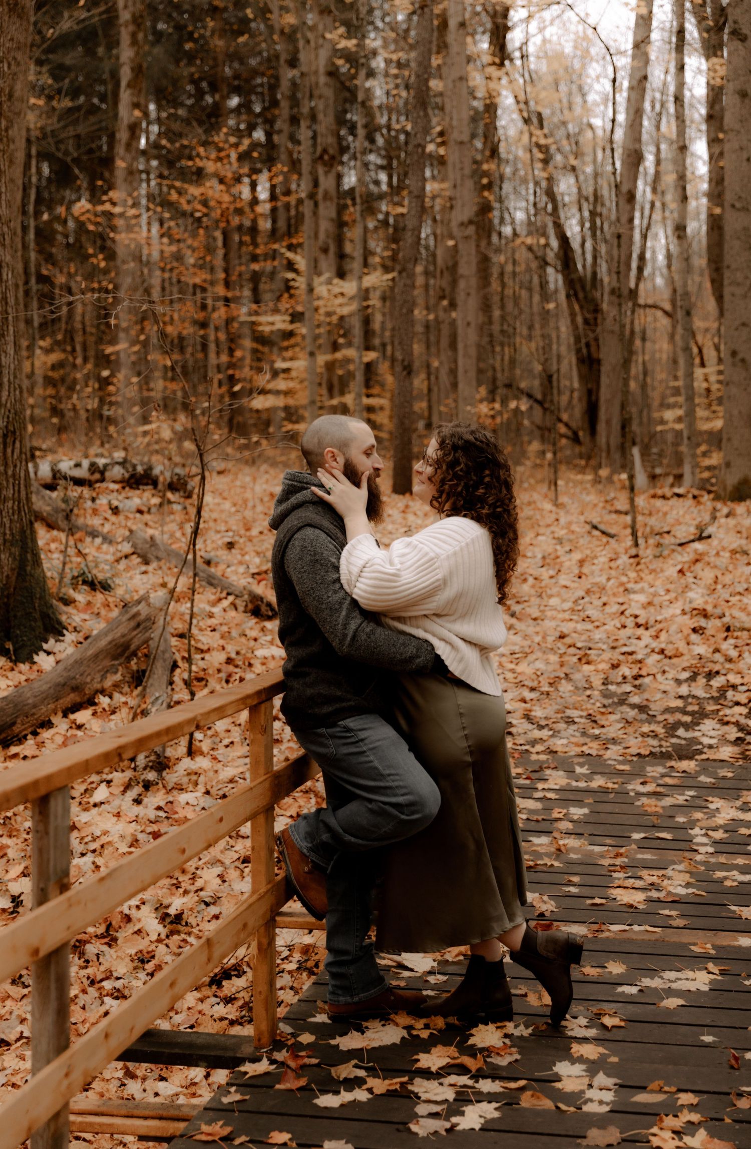 Couple sharing a romantic moment on a leaf-covered wooden walkway in autumn woods.
