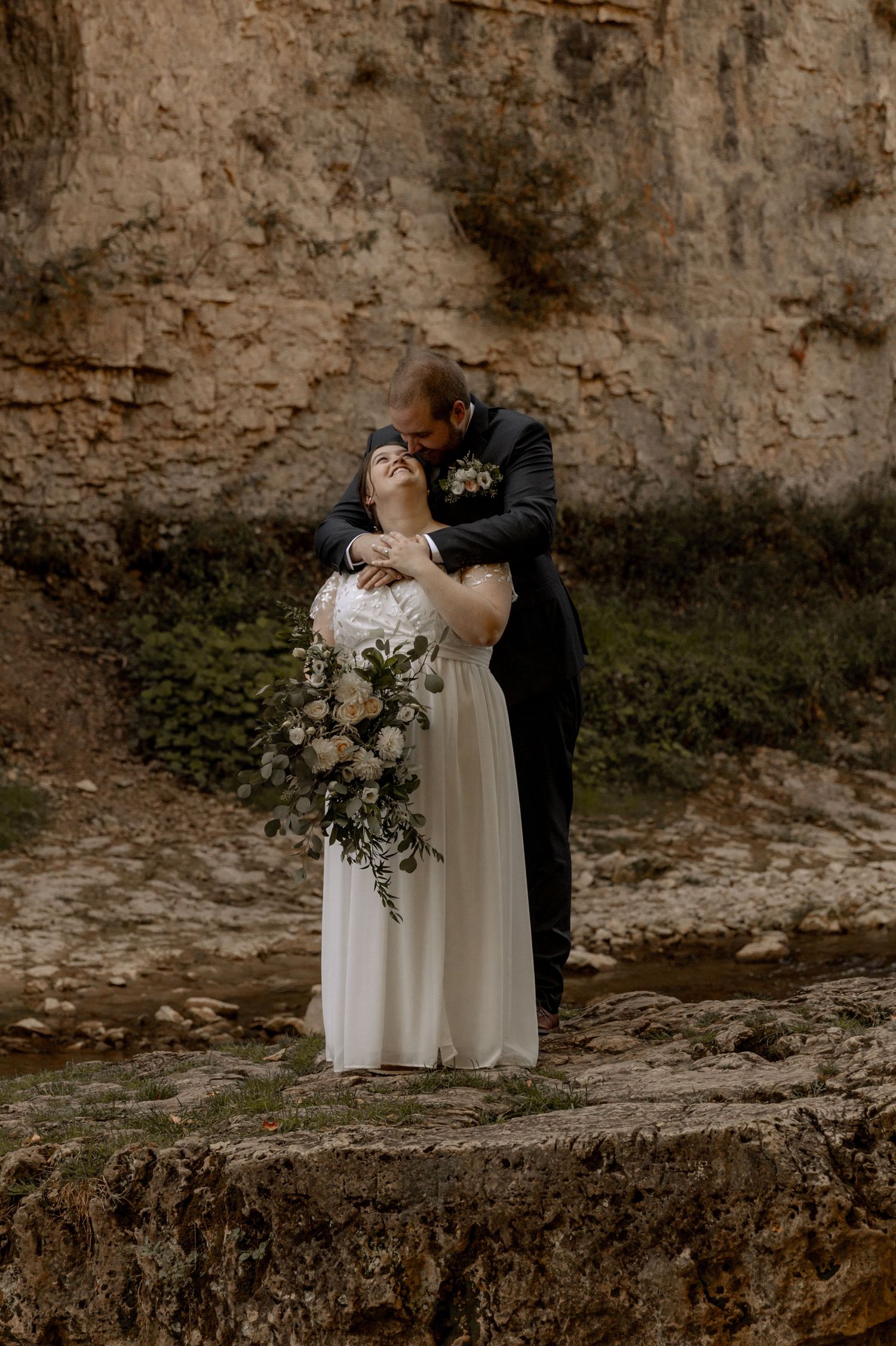 A romantic wedding portrait against a weathered stone wall with a beautiful floral bouquet.