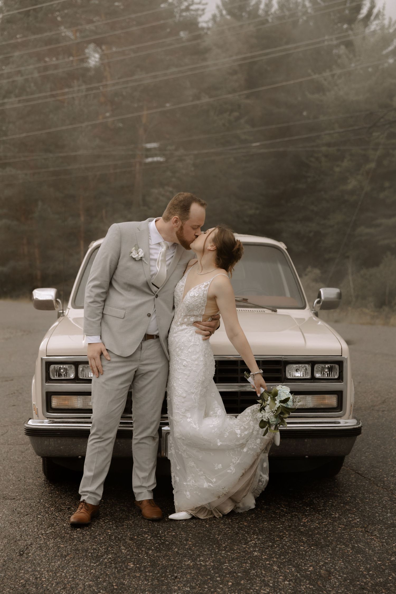 Artistic wedding photo featuring a couple leaning against a vintage truck in muted tones.