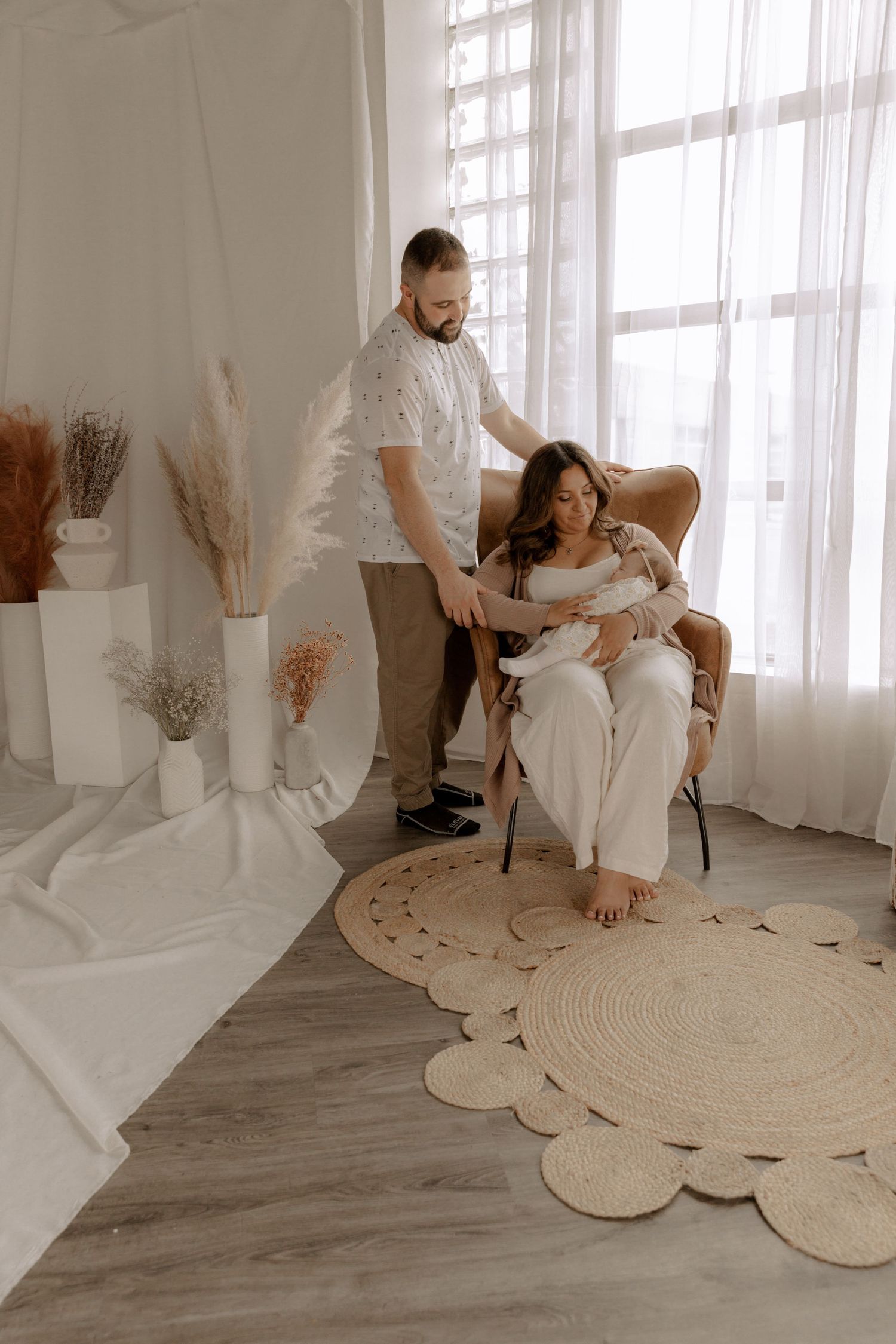 A family relaxing together in a bright minimalist room with a circular patterned rug and dried floral accents.