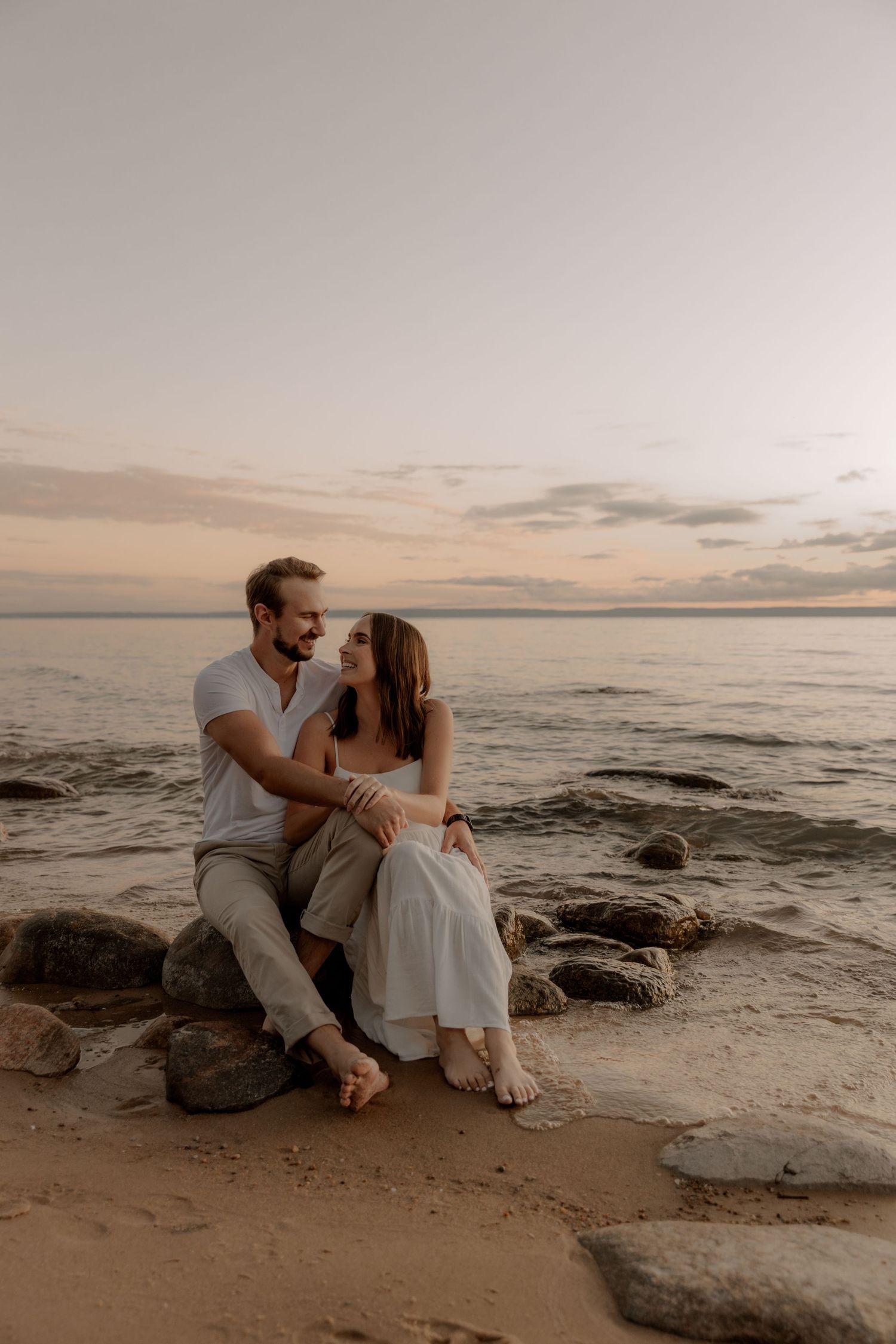 Couple sharing tender moment on rocky shoreline at dusk.