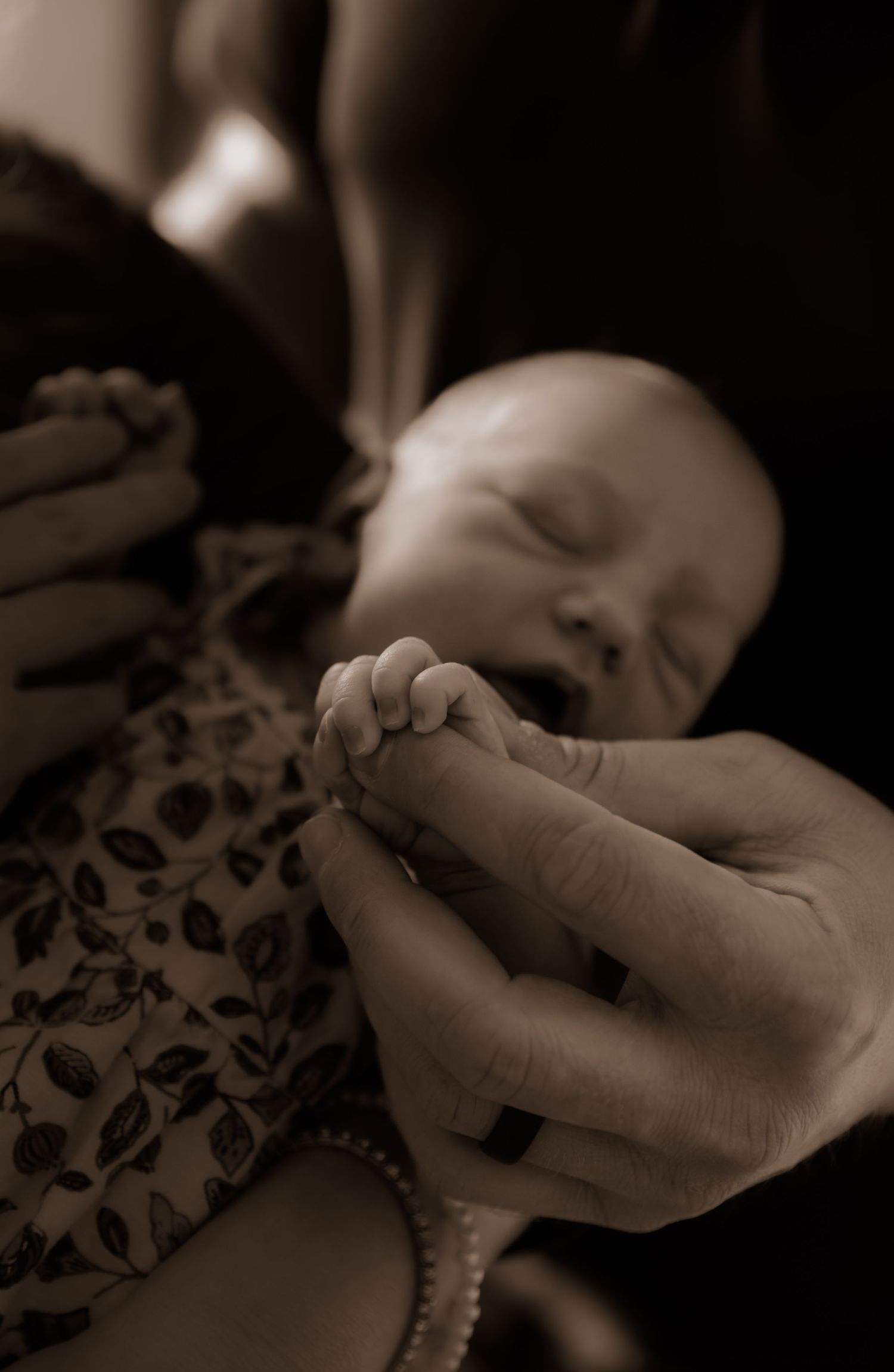 Close-up of tiny infant hand being held against a floral patterned outfit.