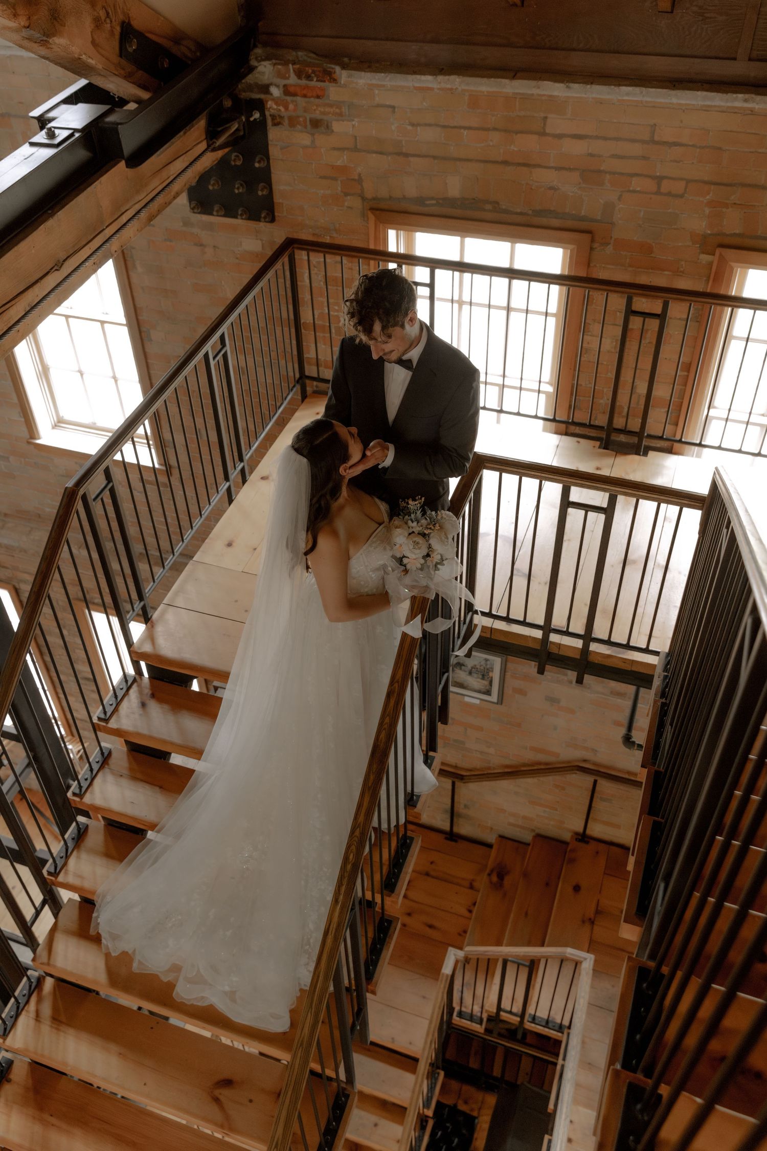 Aerial view of a wedding couple sharing a tender moment on an industrial-style staircase.