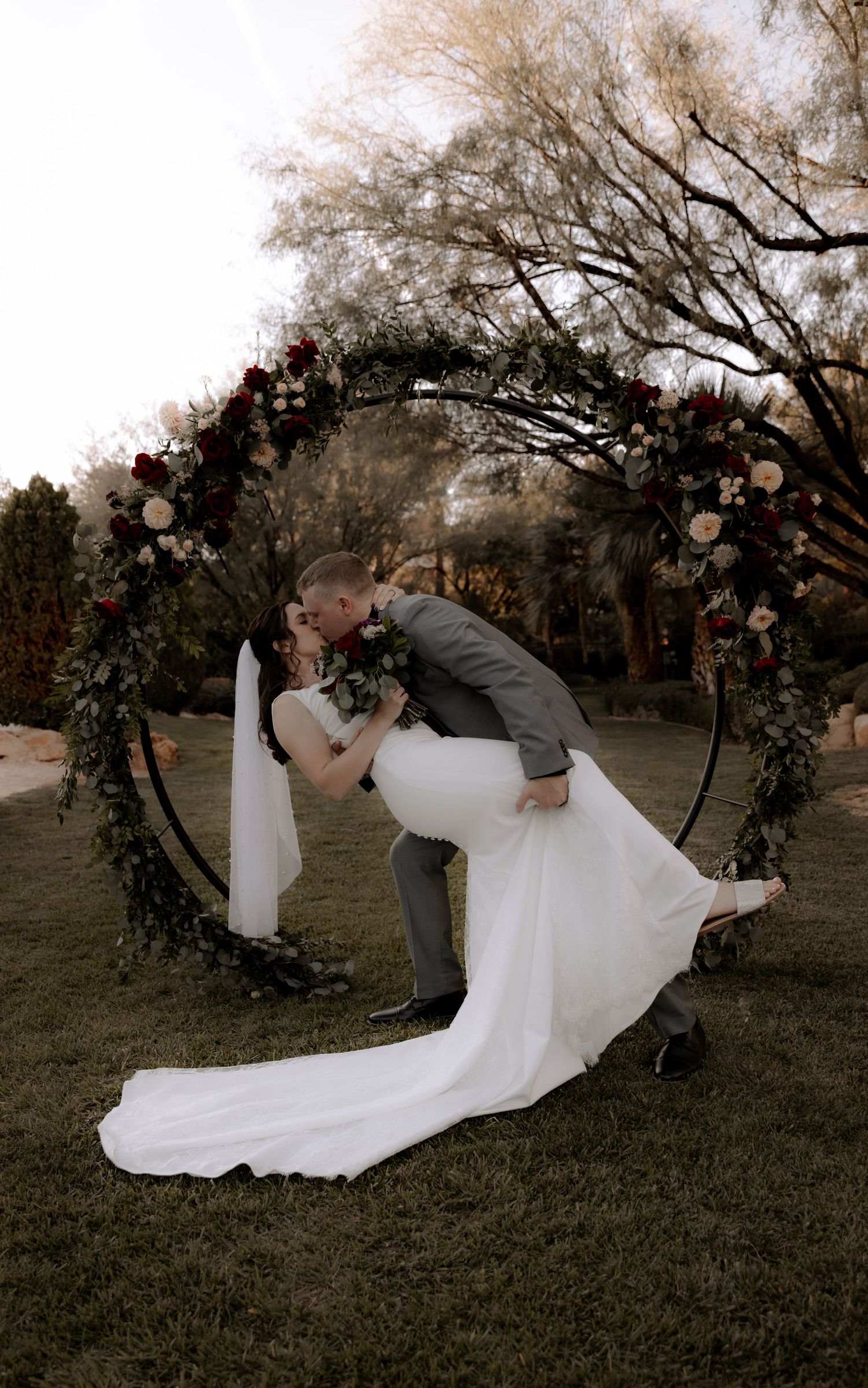 A romantic dip kiss under a floral arch during golden hour.