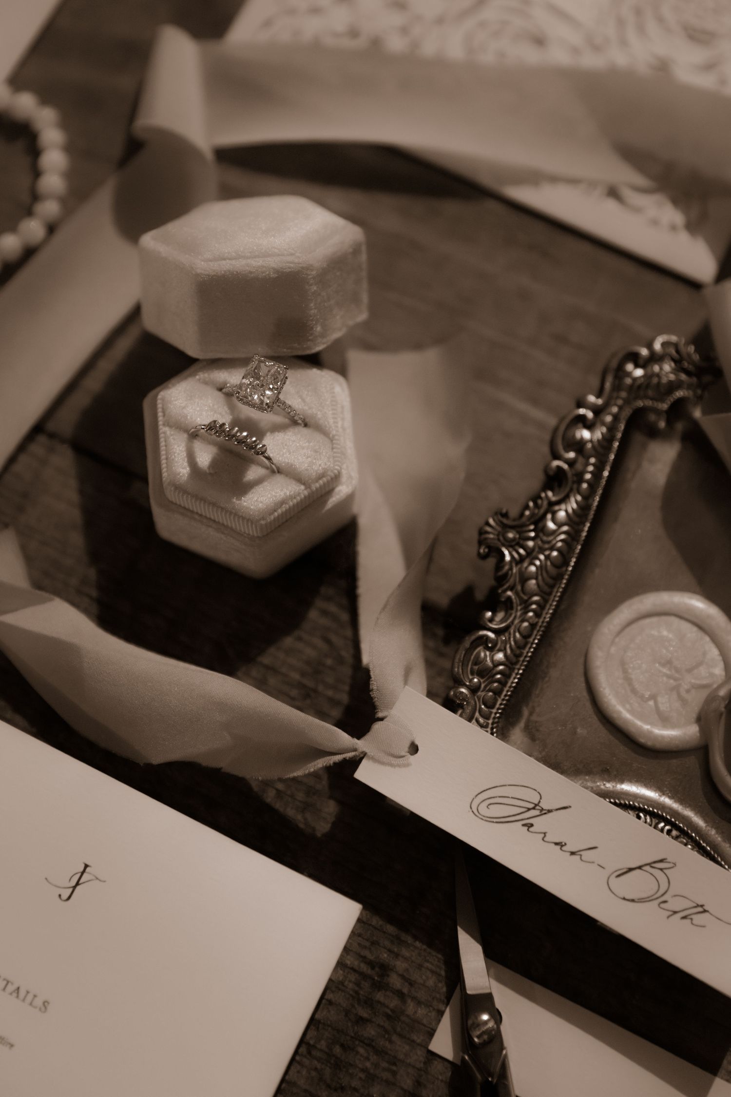 Wedding details display featuring engagement ring box, ornate frame and handwritten cards in sepia tones.