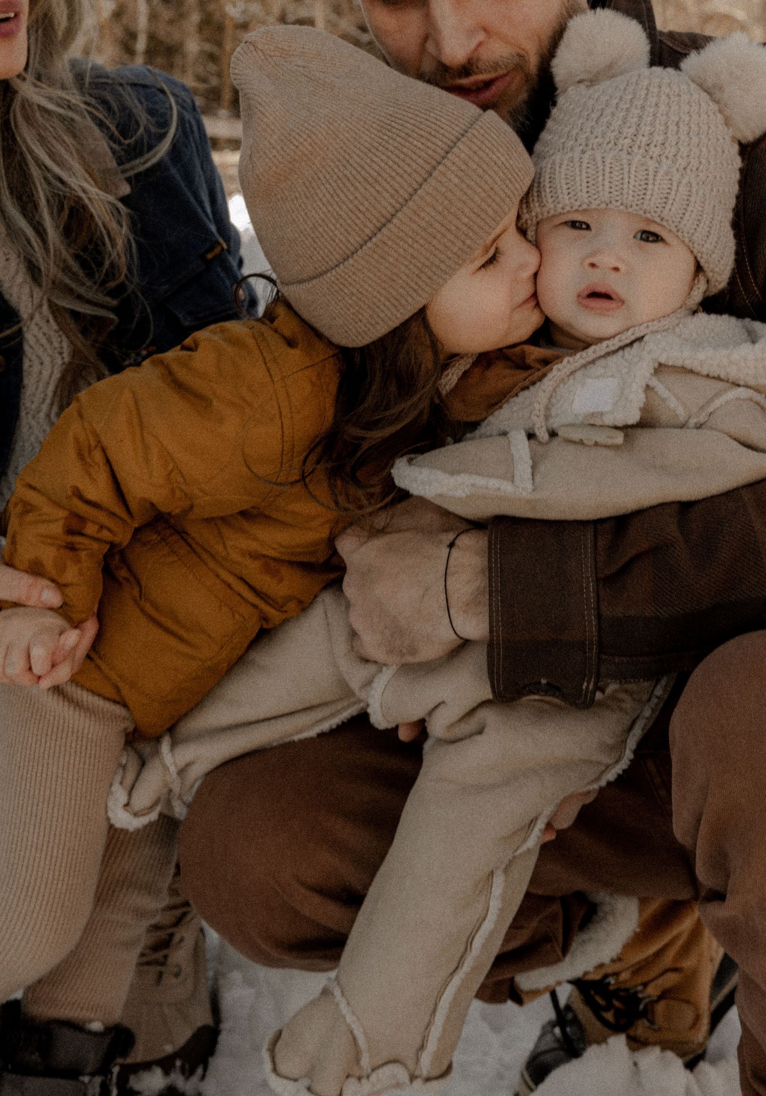 A cozy winter scene shows a family wearing warm knit beanies and outerwear in soft neutral tones.