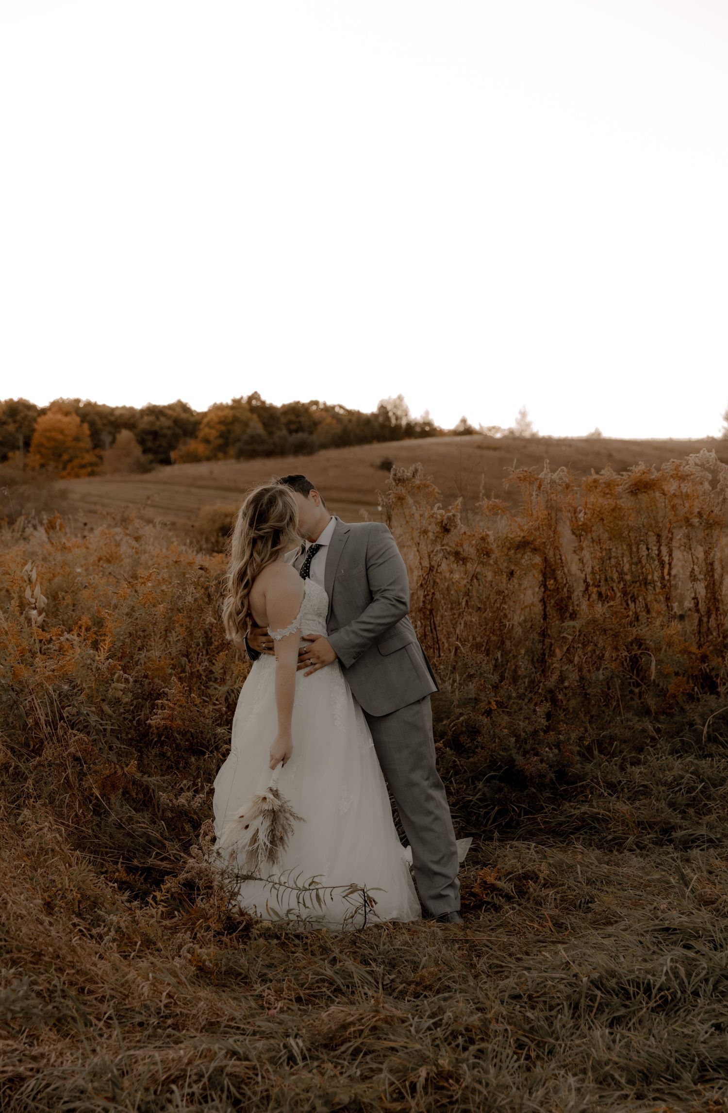Romantic sunset wedding portrait in a rustic field with warm autumn tones.