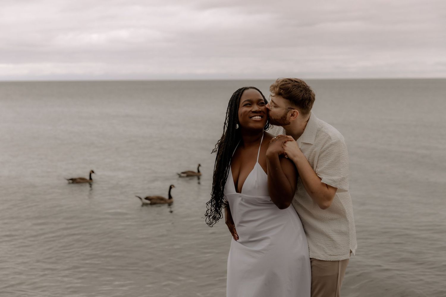 A romantic beachside moment with two people and geese swimming in the background.