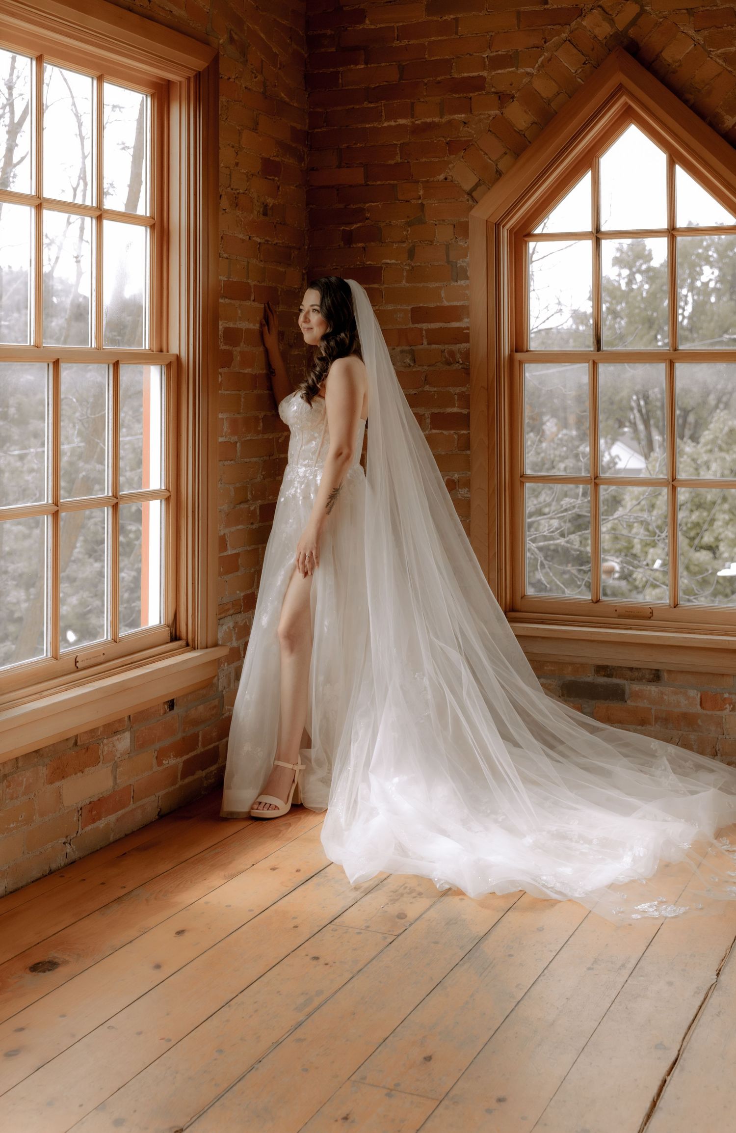 Ethereal bridal portrait with flowing veil in sunlit brick chapel interior.