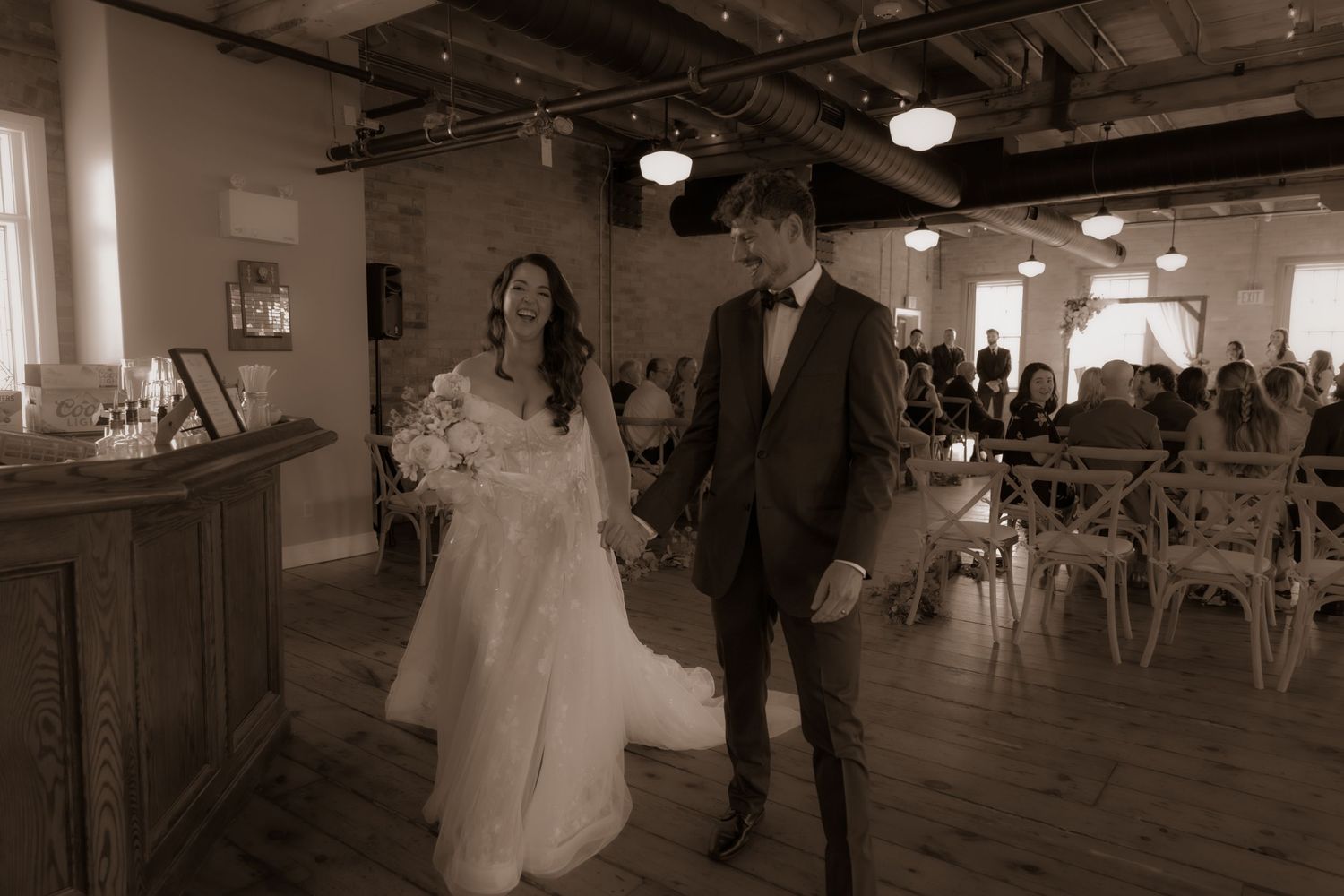 A vintage-style wedding photo showing a couple walking together in a rustic reception venue.