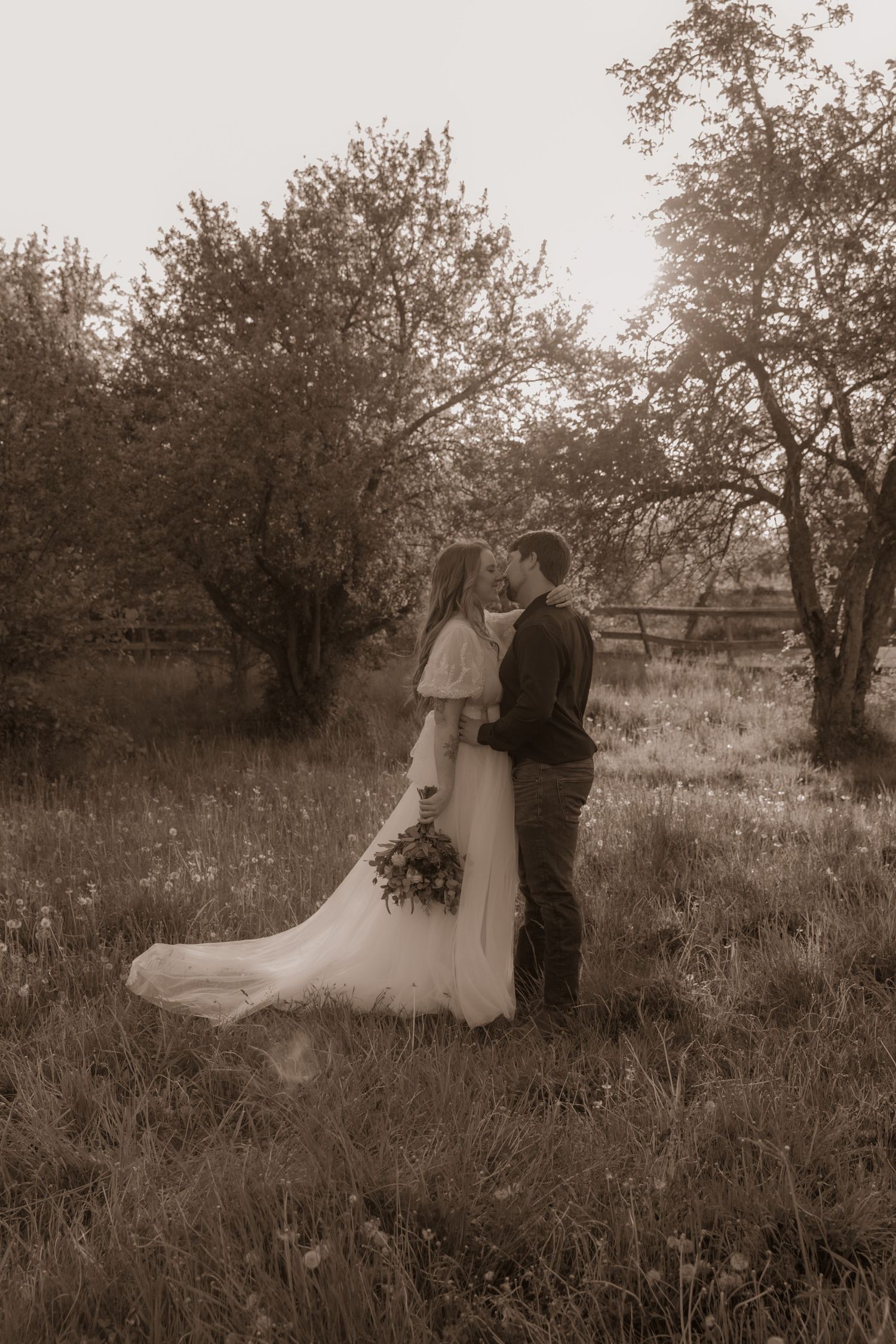 Vintage-style wedding portrait of a couple standing among trees in a rustic setting.