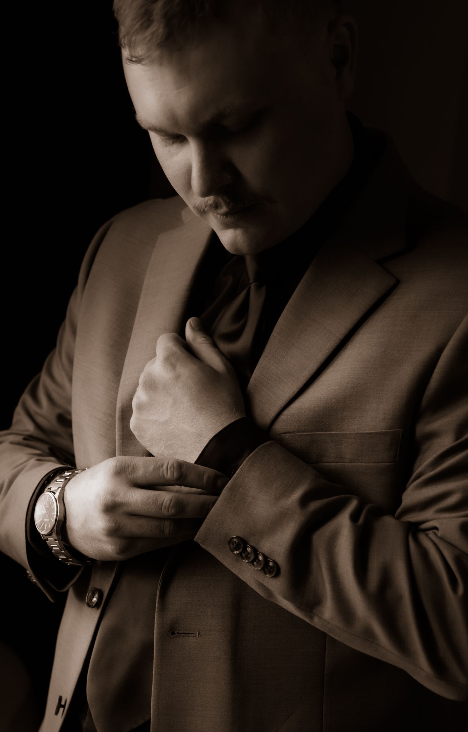A moody sepia portrait of a suited figure adjusting their tie against a dark background.