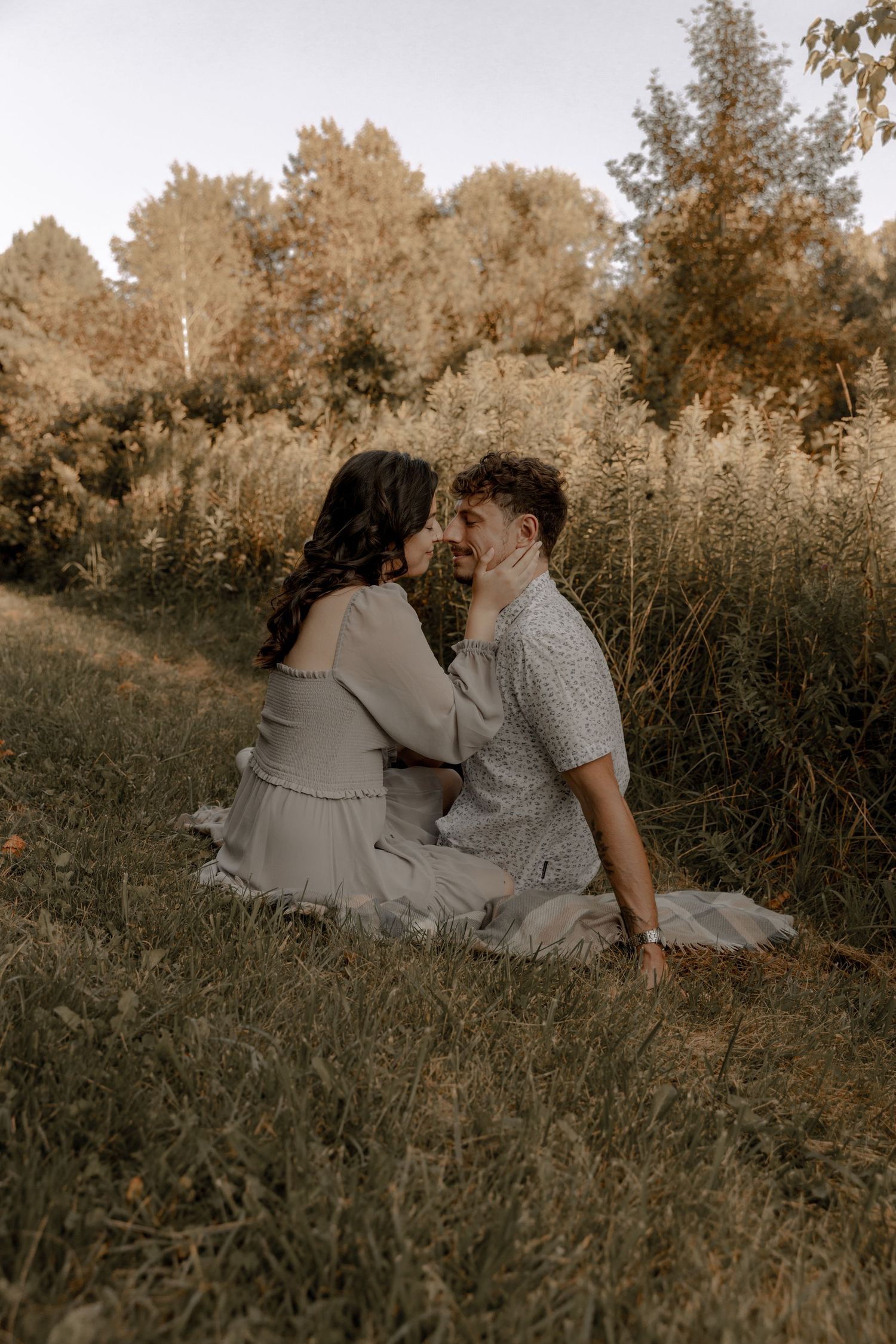 A couple sharing a tender moment while sitting in tall grass during golden hour.