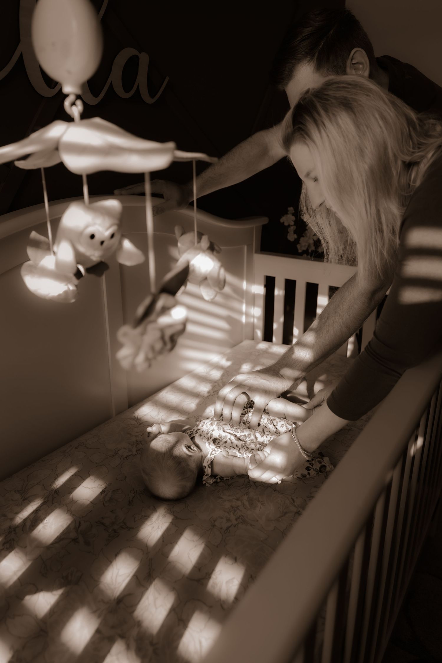 Nursery mobile casts shadows over a crib while being adjusted in sepia lighting.