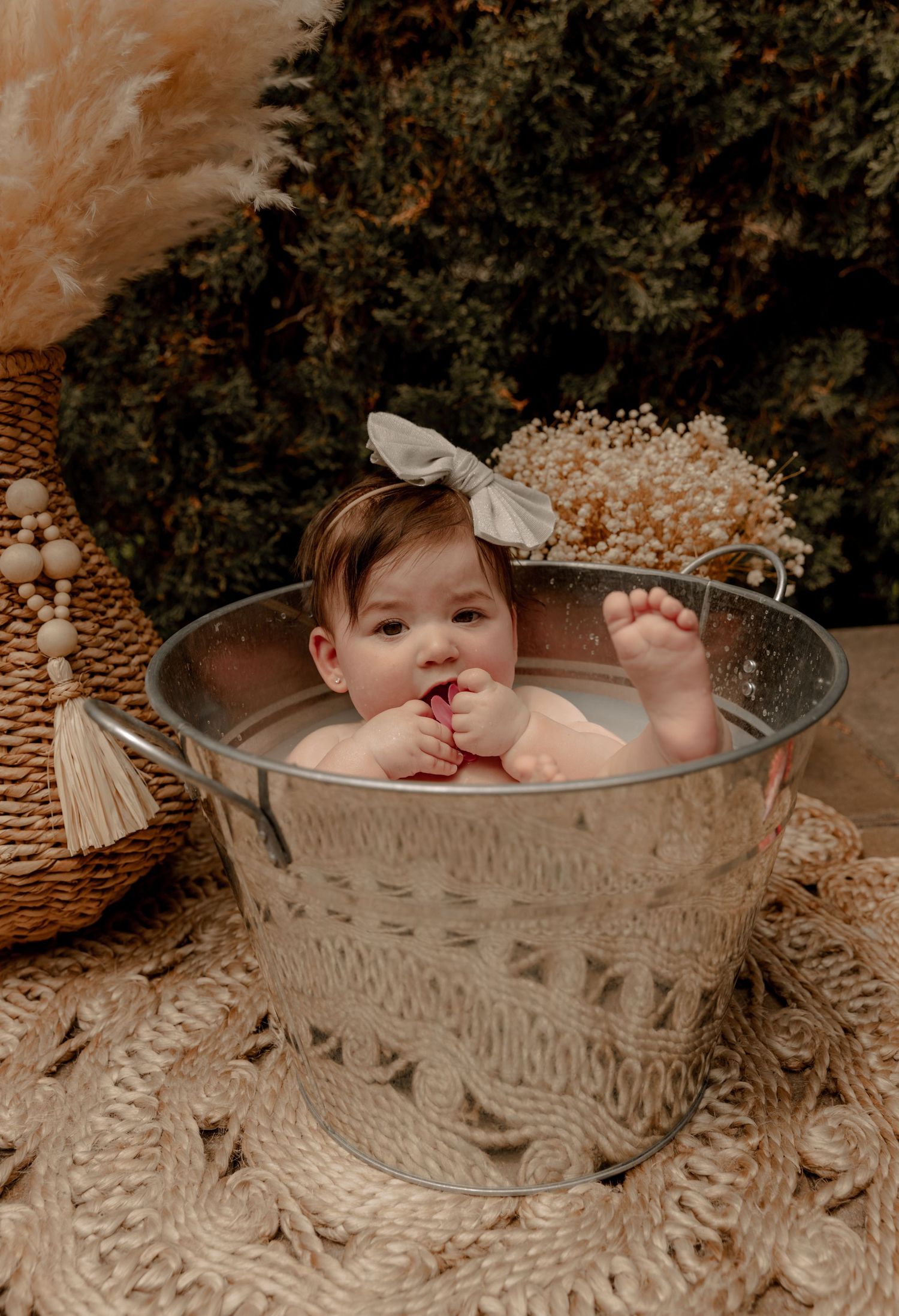 A baby sits in an antique metal wash tub surrounded by dried flowers and boho decor in a vintage-style photoshoot.