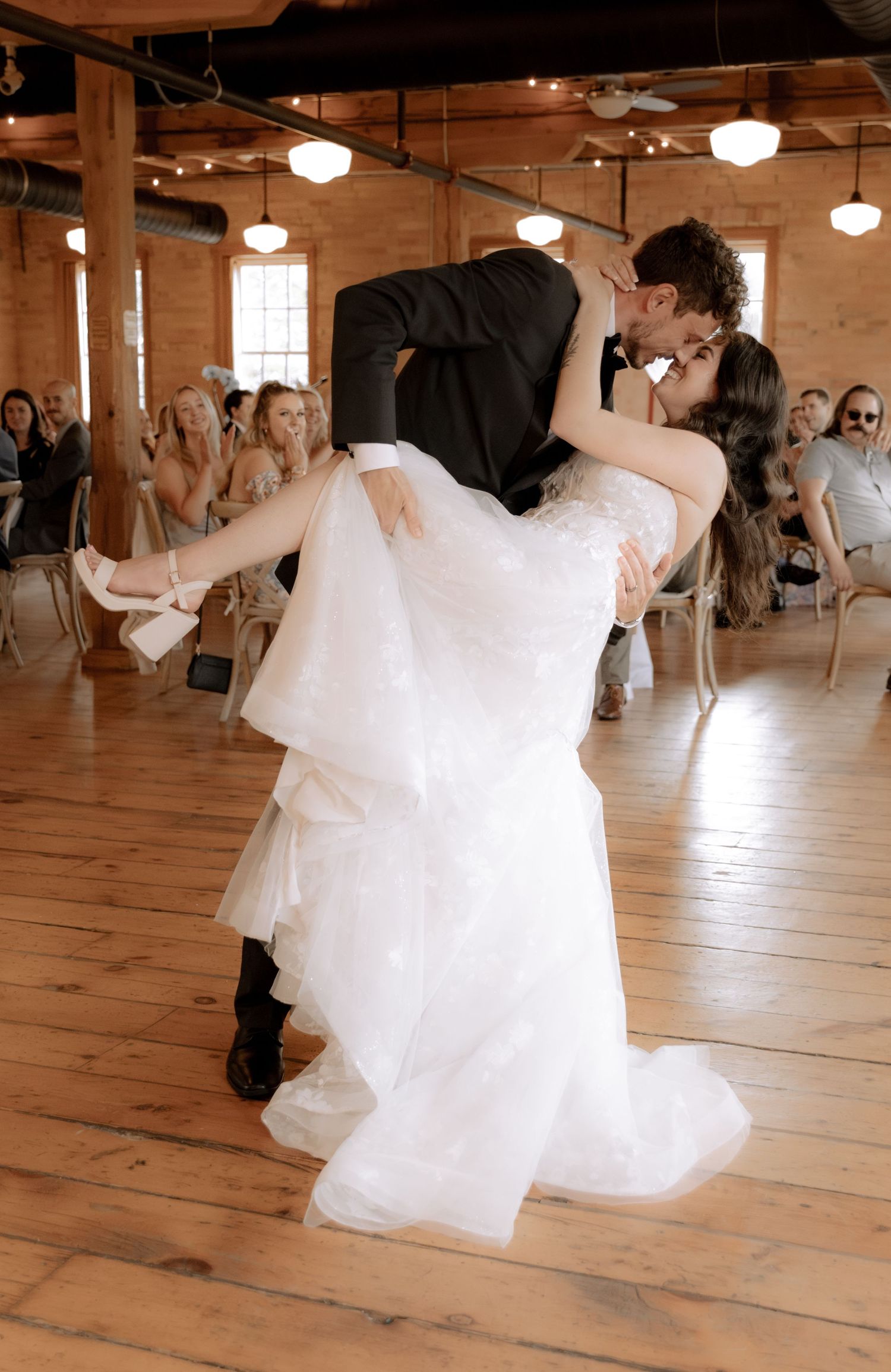 Newlyweds perform a romantic dip during their wedding dance on a polished wooden floor.
