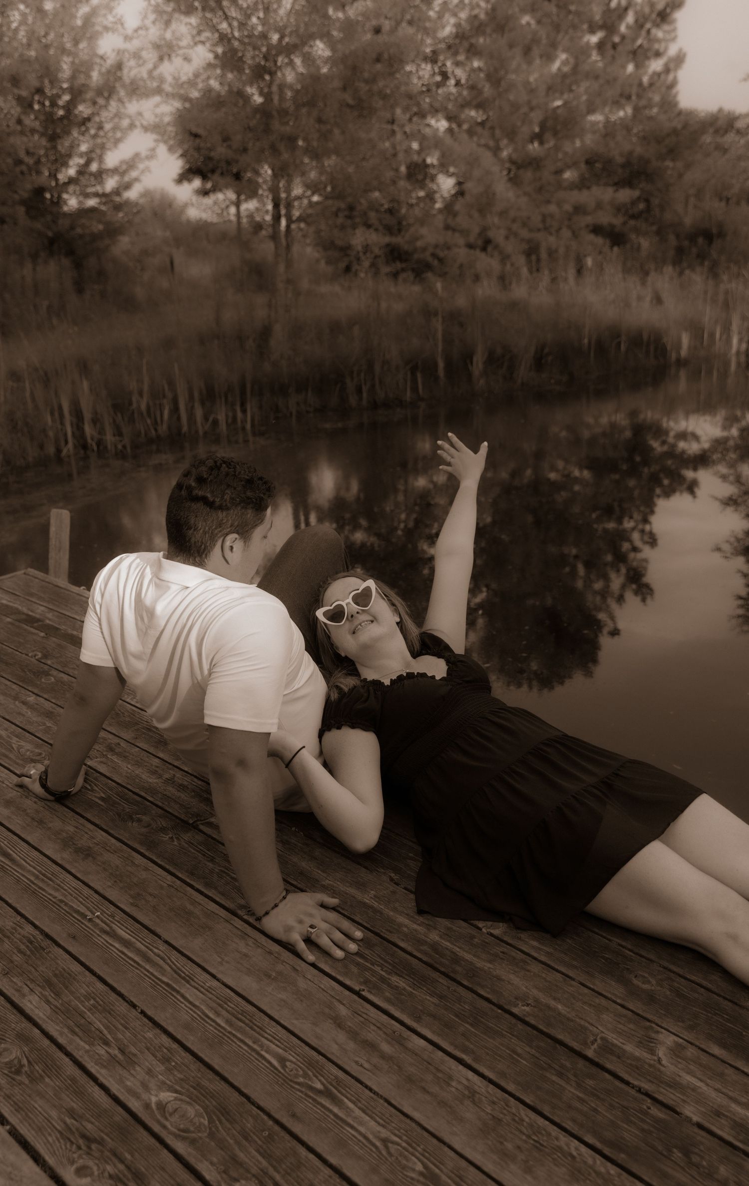 A couple enjoying a romantic moment together on a wooden dock by a serene pond in vintage sepia tones.