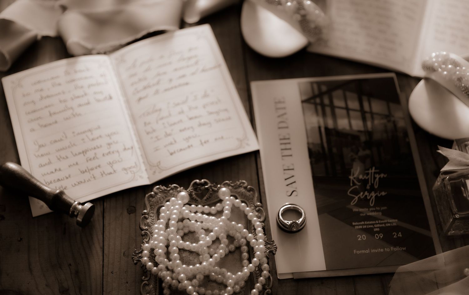 Wedding flat lay with handwritten journal, pearl necklace, and invitation in sepia tones.