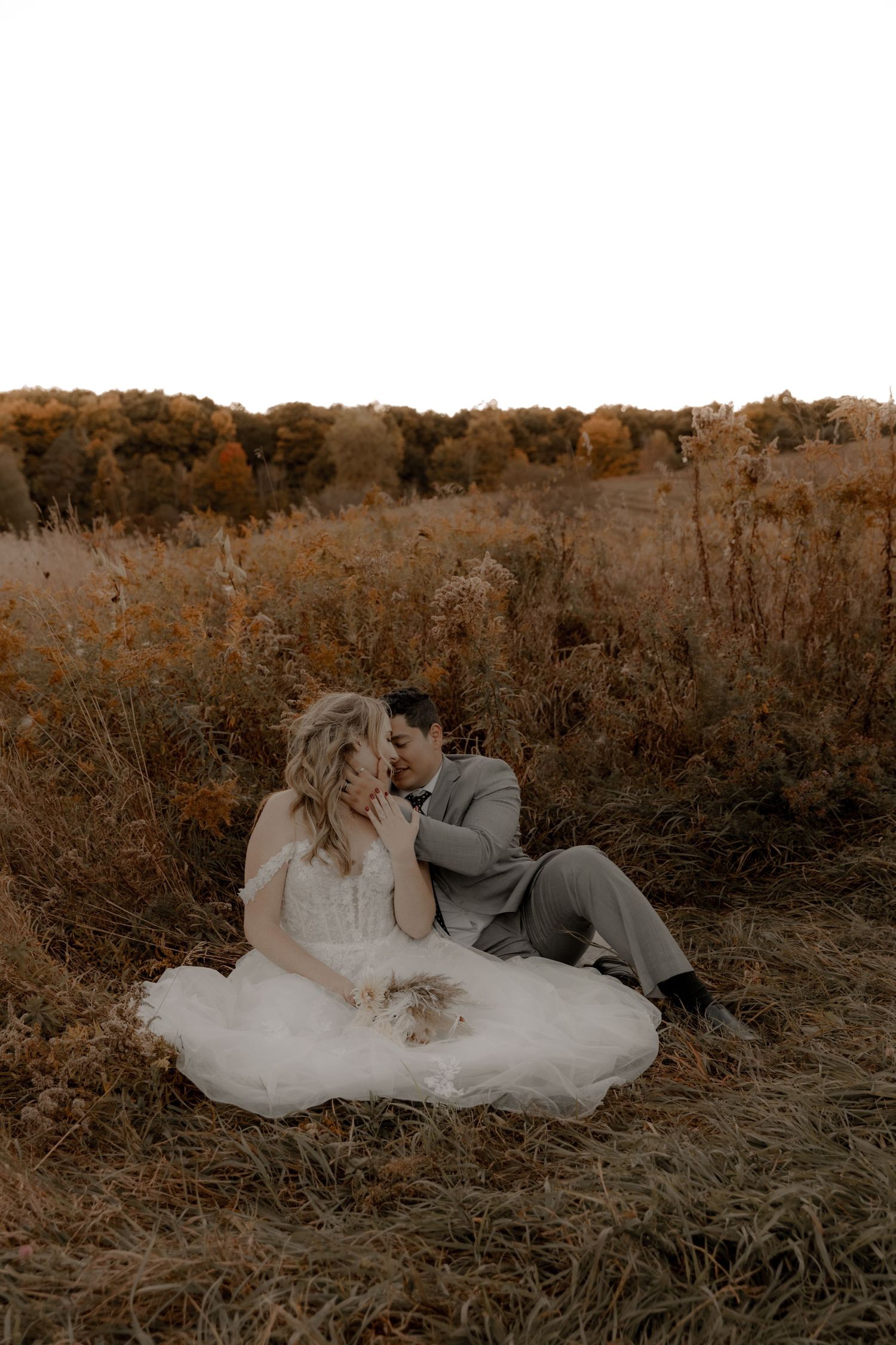 A warm-toned wedding portrait featuring a couple in a rustic autumn setting.