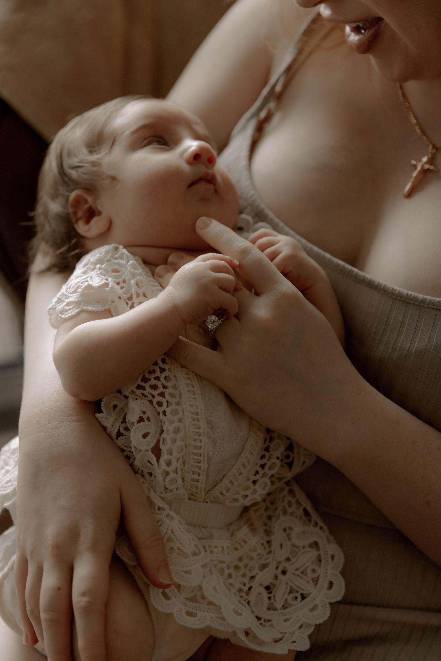 Close-up sepia photo of a baby wearing white lace dress while resting with gentle caring hands touching.