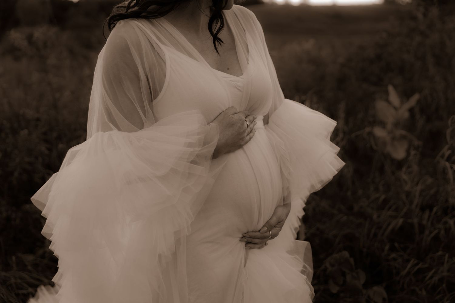 A black and white photo shows a flowing white dress with sheer fabric moving in a dramatic fashion in a meadow.