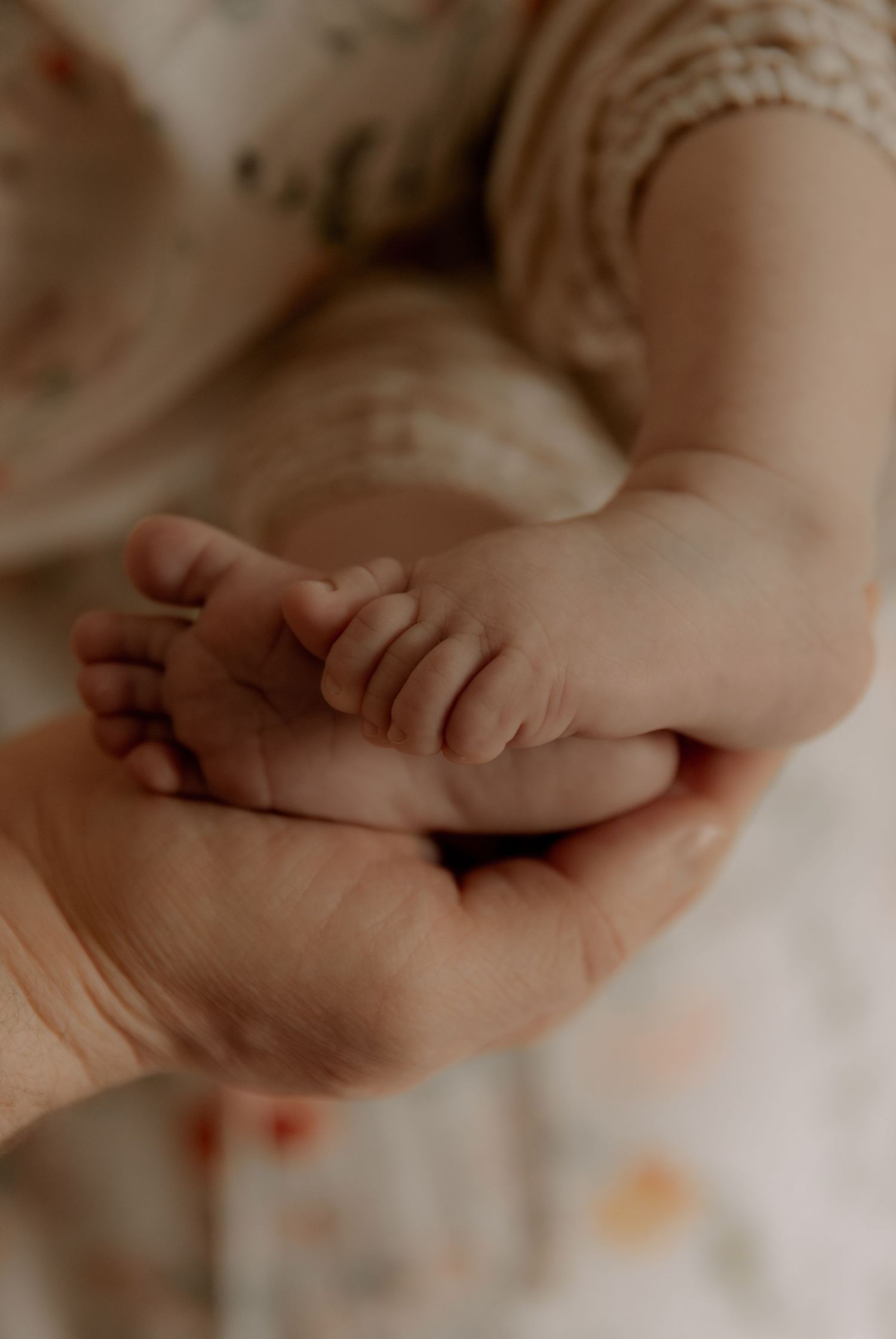 A small baby's hand gently rests in an adult's palm against a soft white background.