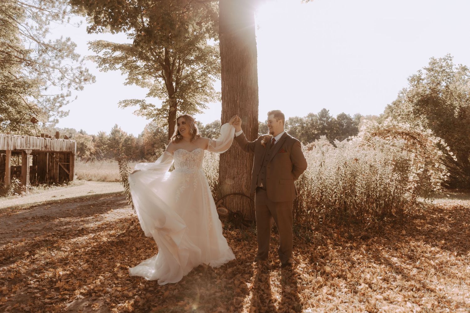Newly married couple poses in warm autumn light with trees and tall grass creating a romantic backdrop.