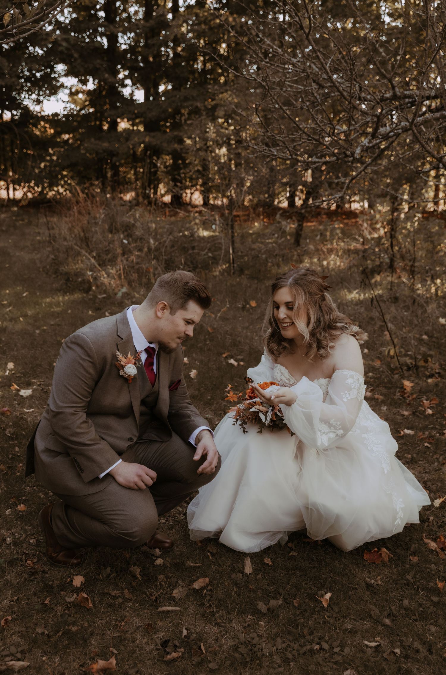 A bride and groom in traditional wedding attire share a quiet moment among fall foliage.