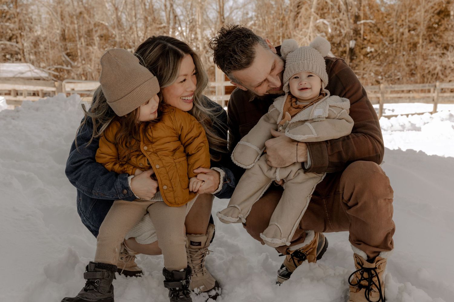 Group sitting together in snowy winter landscape wearing cozy outerwear in warm earth tones.